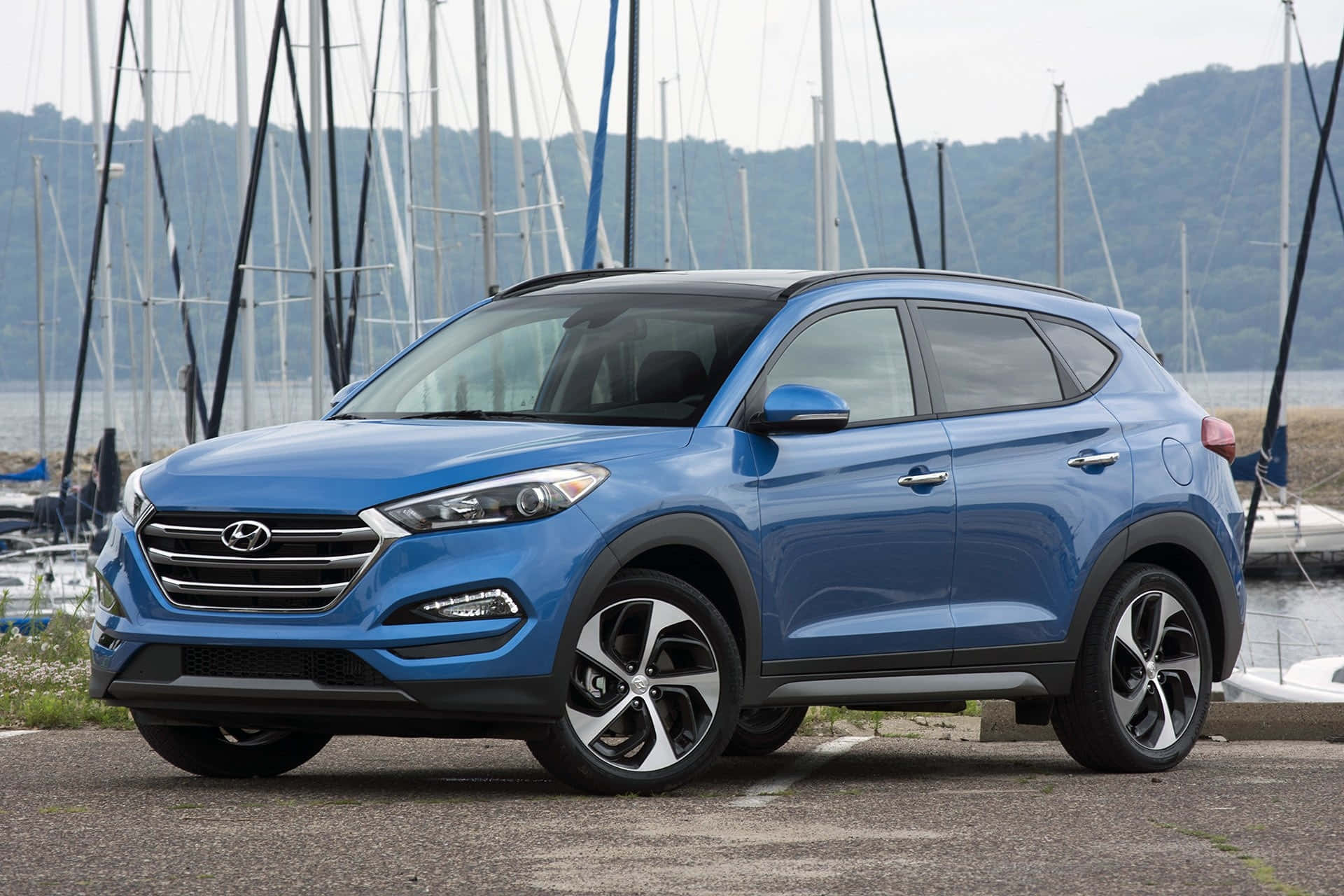 Hyundai Tucson 桌布 壁紙 — 一輛鮮藍色的現代Tucson SUV停泊在碼頭，背景有帆船和山丘。