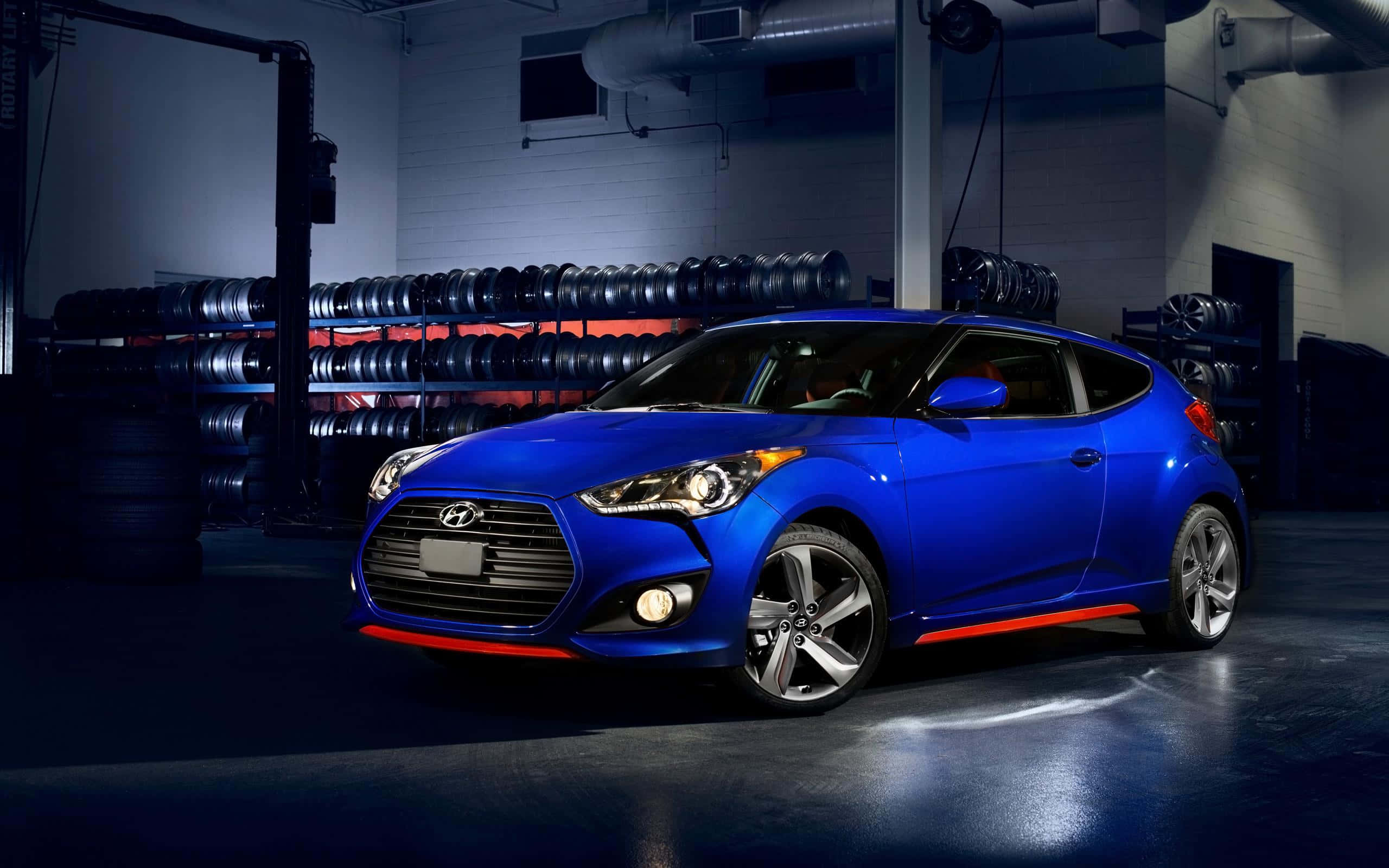 Hyundai Veloster 桌布 壁紙 — 一輛充滿活力的藍色現代Veloster，帶有紅色點綴，在堆滿輪胎的昏暗車庫中，於攝影棚燈光下閃閃發光。