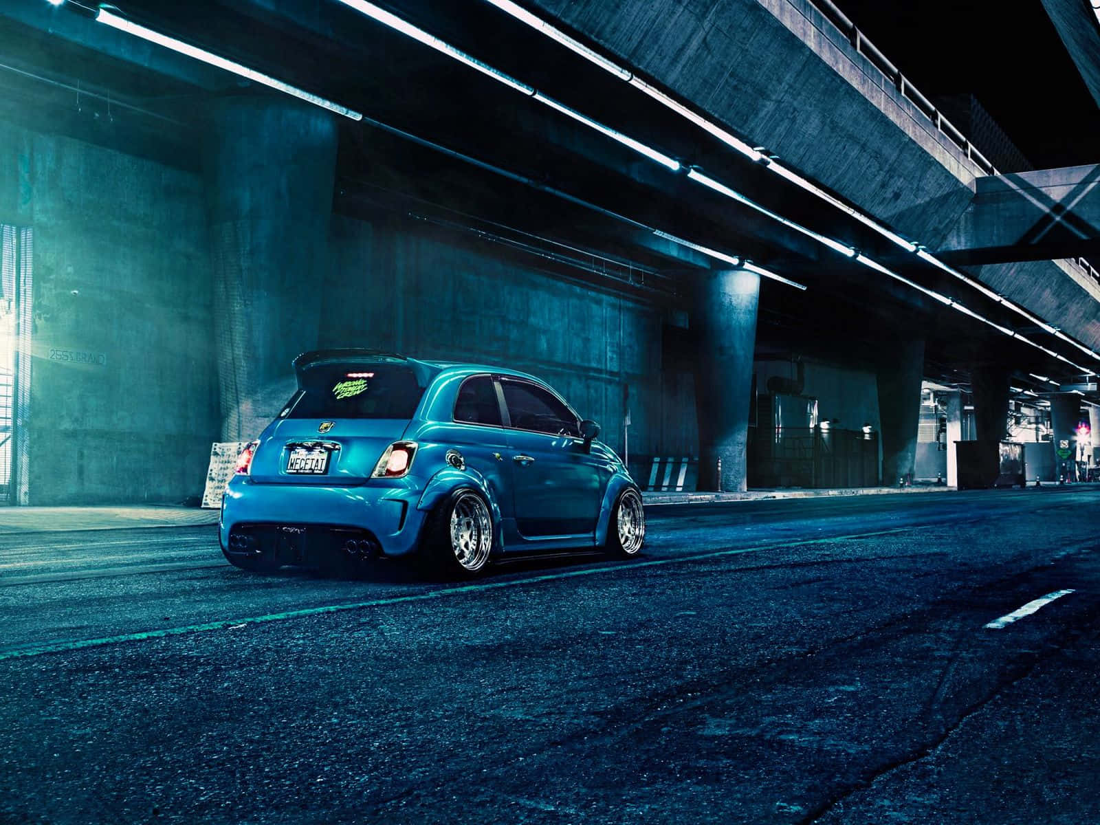 Fiat 500l 桌布 壁紙 — 一輛鮮藍色改裝的Fiat 500在夜間停泊在混凝土天橋下，被霓虹燈照亮。