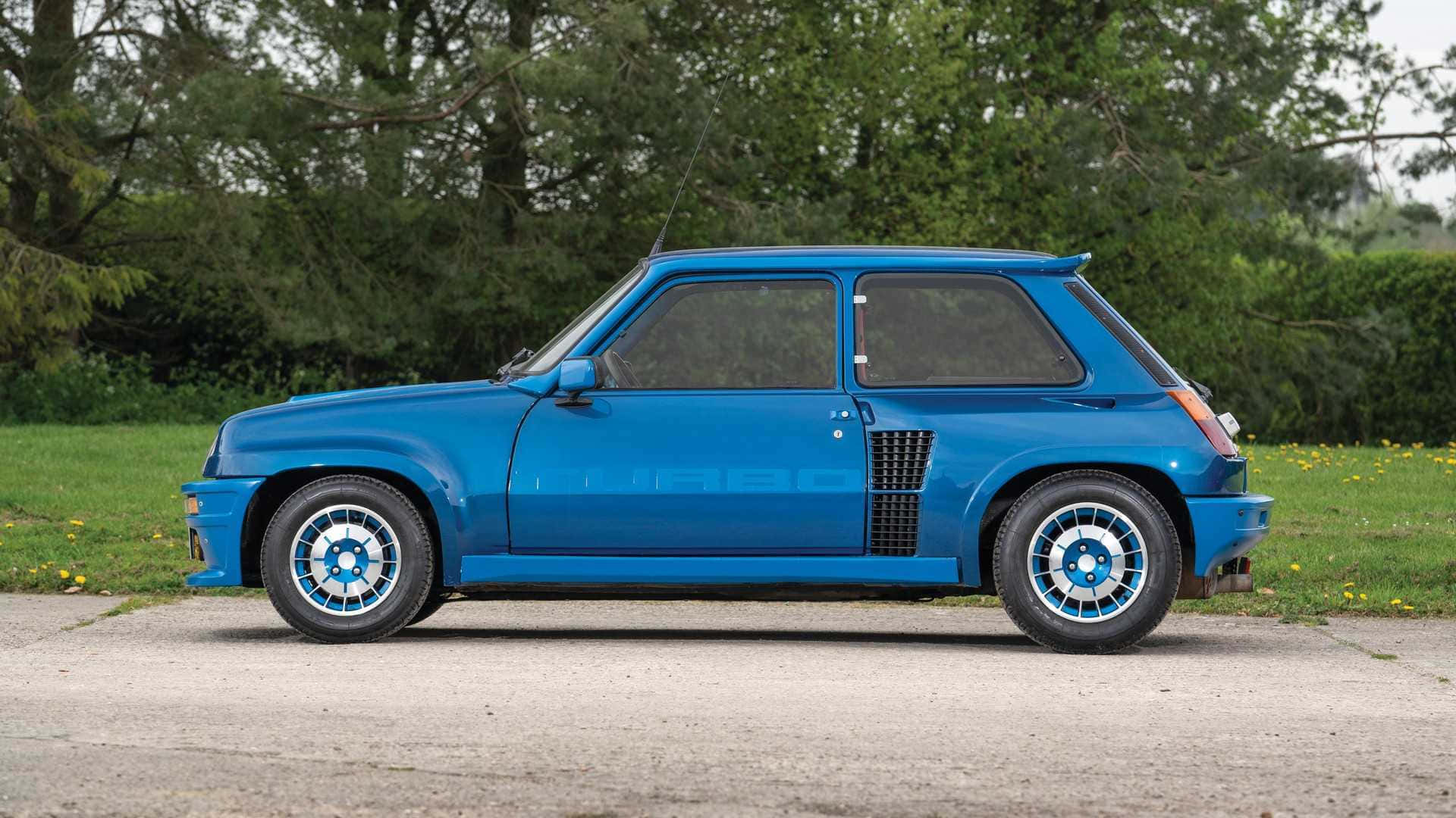 Renault 5 Turbo 桌布 壁紙 — 一輛充滿活力的藍色雷諾5 Turbo 2跑車停泊在碎石路上，旁邊是草地，背景有樹木。