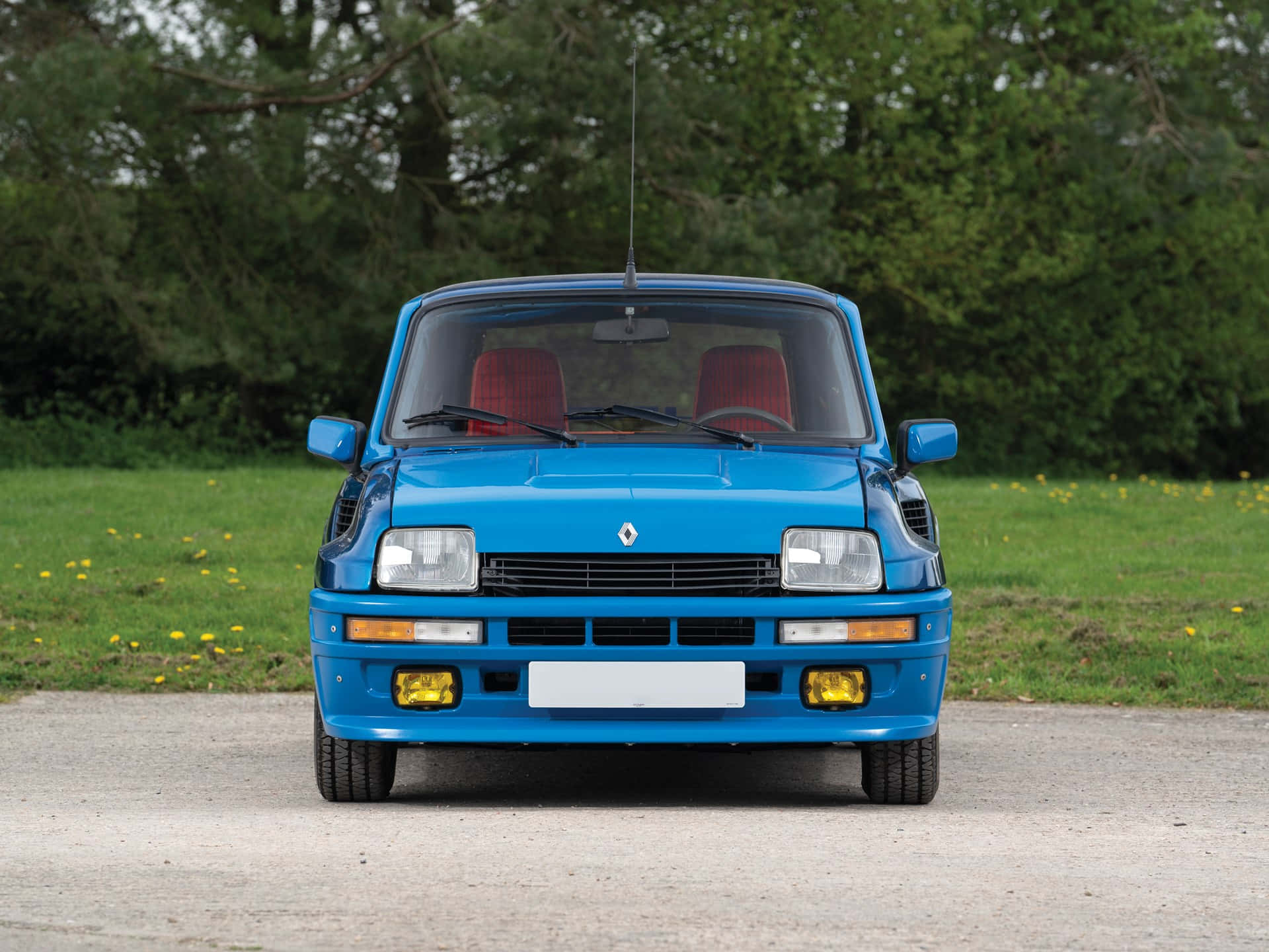 Renault 5 Turbo 桌布 壁紙 — 一輛鮮藍色的雷諾5 Turbo正面朝向碎石路，背景有綠色草地和樹木。