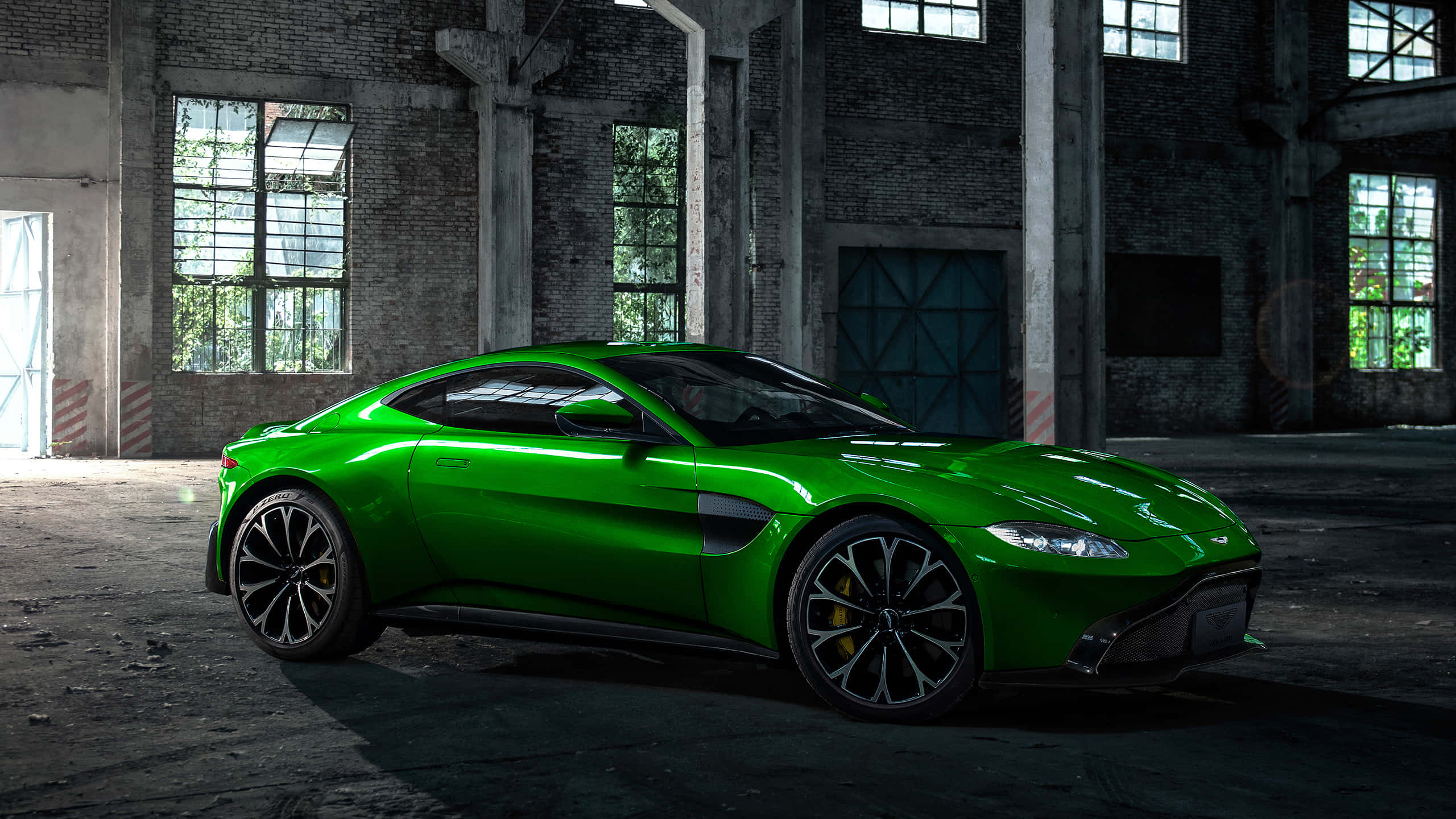 Aston Martin Vantage 桌布 壁紙 — 一輛充滿活力的綠色跑車在自然光線透過破爛窗戶照射進一個骯髒廢棄倉庫中閃閃發光。