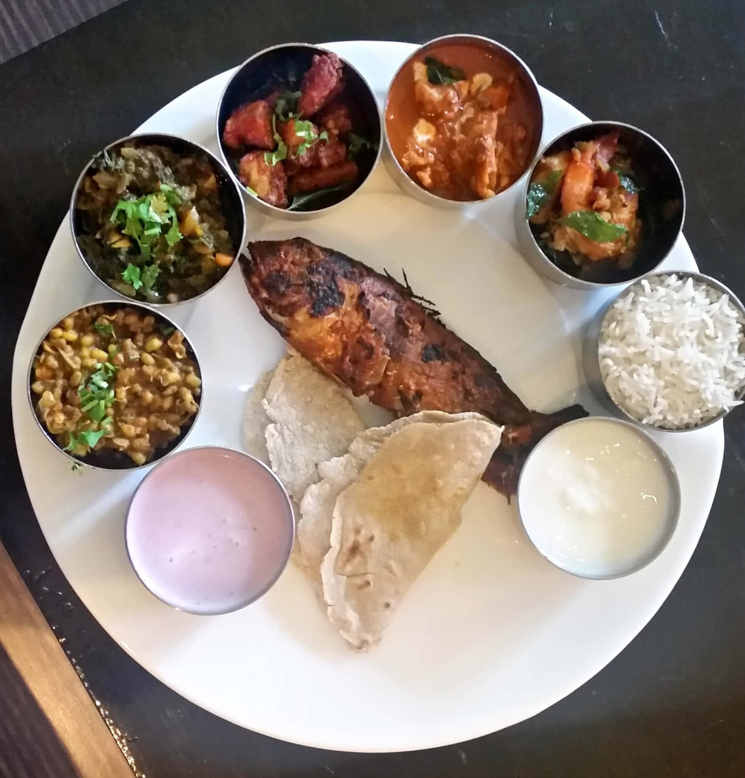 Thali 桌布 壁紙 — 一個充滿活力的印度塔利，包括烤魚煎餅和色彩繽紛的咖哩，盛在金屬碗中，放在白色盤子上。