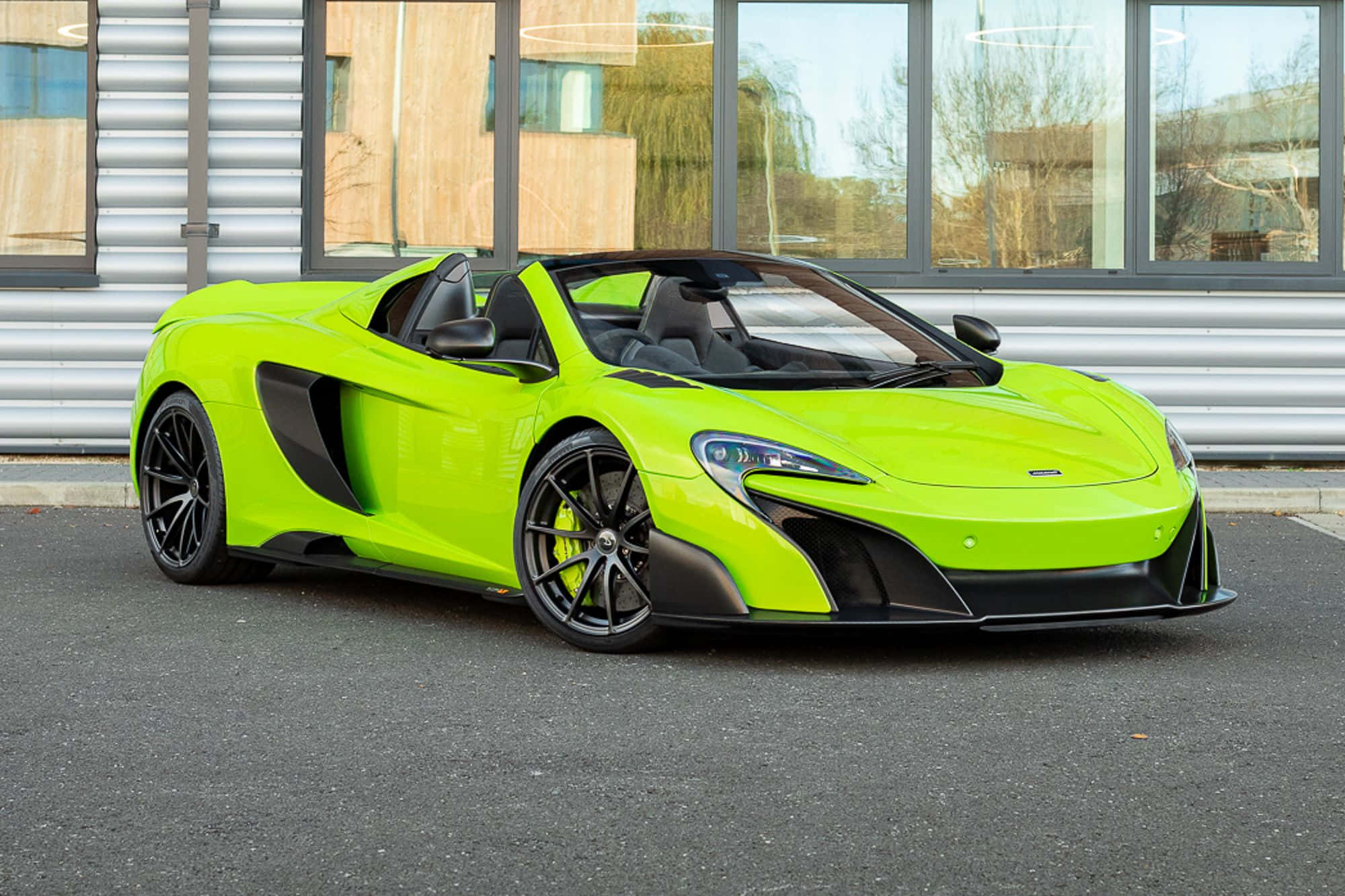 Mclaren 675lt Spider 桌布 壁紙 — 一輛鮮豔的青檸綠色McLaren 570S Spider停泊在瀝青路面上，前方是帶有反光窗戶的現代建築。