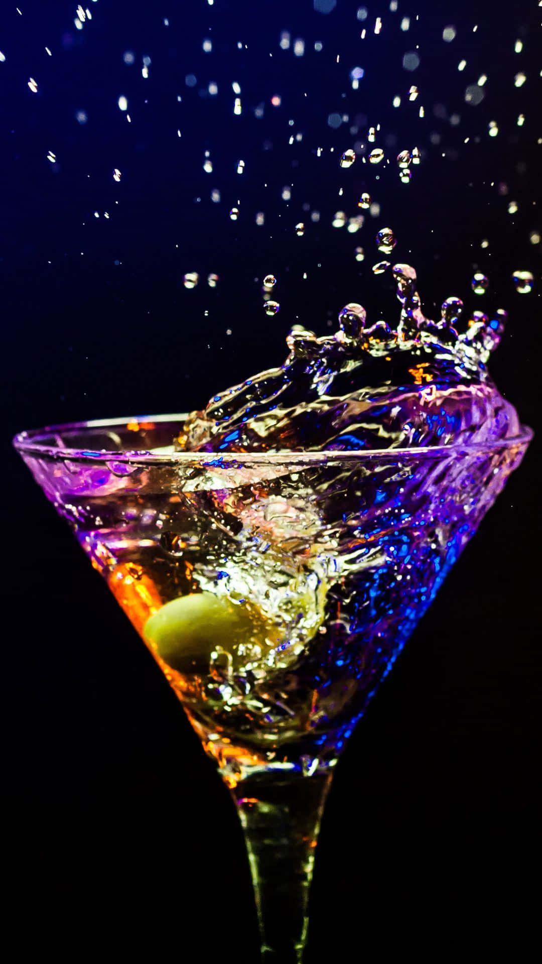  壁紙 — 一個充滿活力的馬提尼杯，內有綠色橄欖，在深色背景下濺起彩虹色的液體。