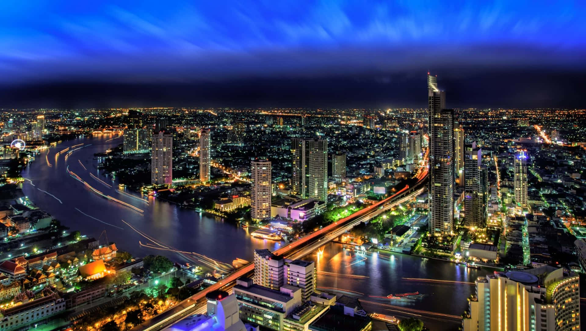  壁紙 — 充滿活力的夜景，閃爍的摩天大樓和河流在深藍色天空下反射霓虹燈光。