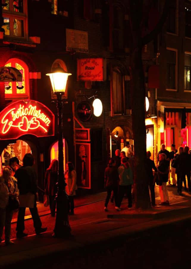 Red Light District 桌布 壁紙 — 充滿活力的夜間街景，沐浴在發光招牌和路燈散發的溫暖紅色霓虹燈光中，行人沿著鵝卵石小徑漫步。