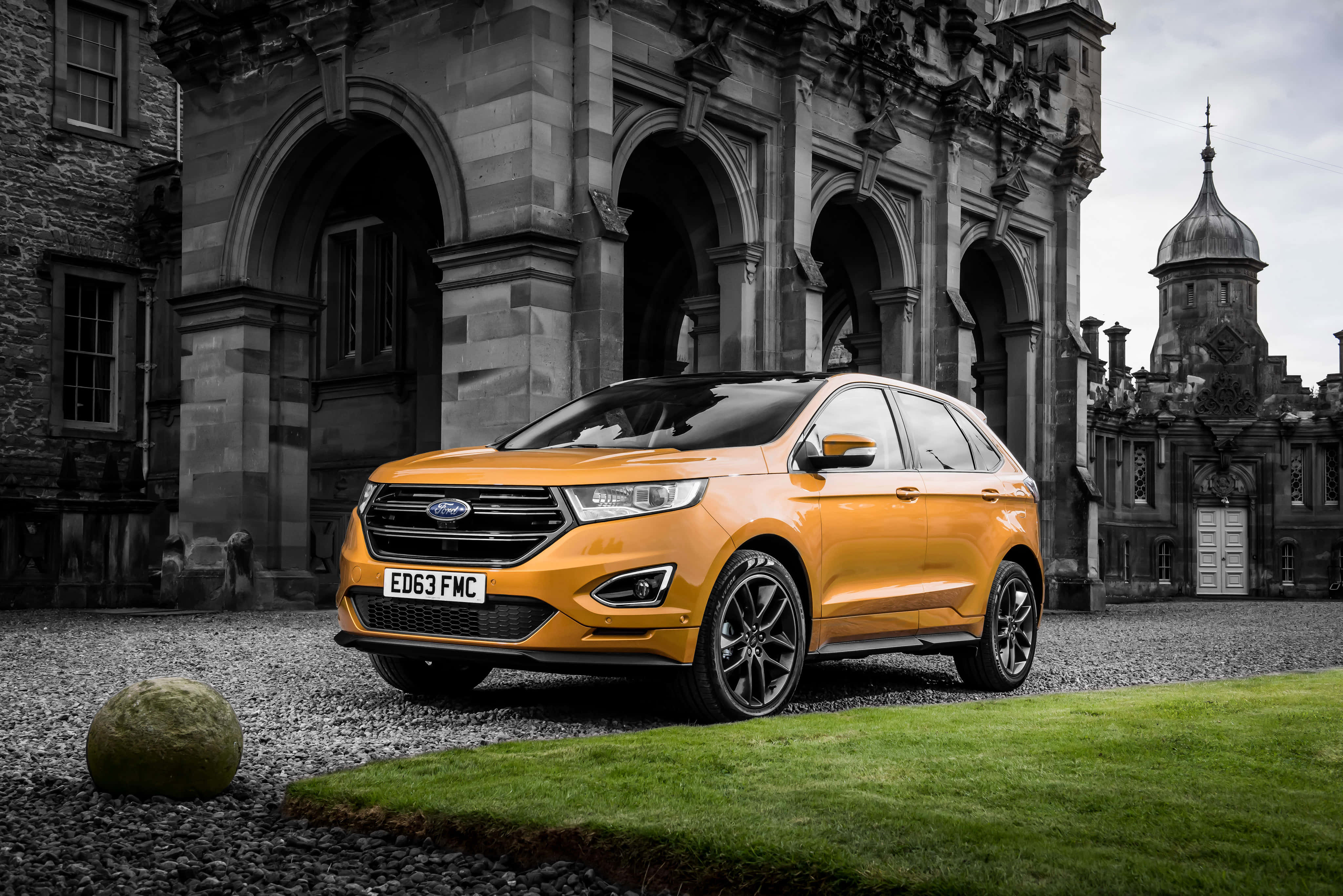 Ford Edge 桌布 壁紙 — 一輛充滿活力的橙色福特Edge SUV停在碎石路上，前方是一座宏偉的歷史石建築，帶有拱形入口。