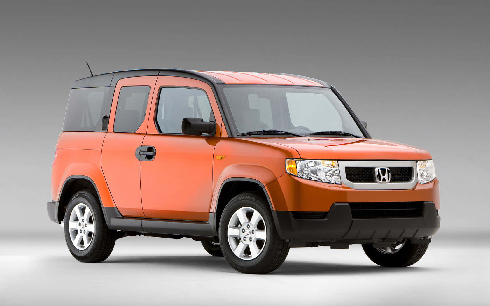 Honda Element 桌布 壁紙 — 一輛充滿活力的橙色本田Element SUV，帶有黑色車頂和飾條，在灰色中性背景的攝影棚中展示。