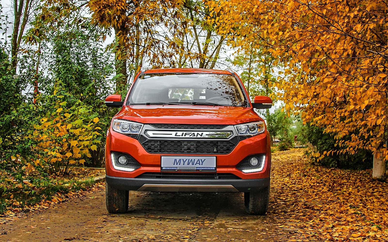  壁紙 — 一輛鮮橙色的力帆MyWay SUV停泊在鋪滿落葉的小徑上，周圍是金黃色的秋樹。