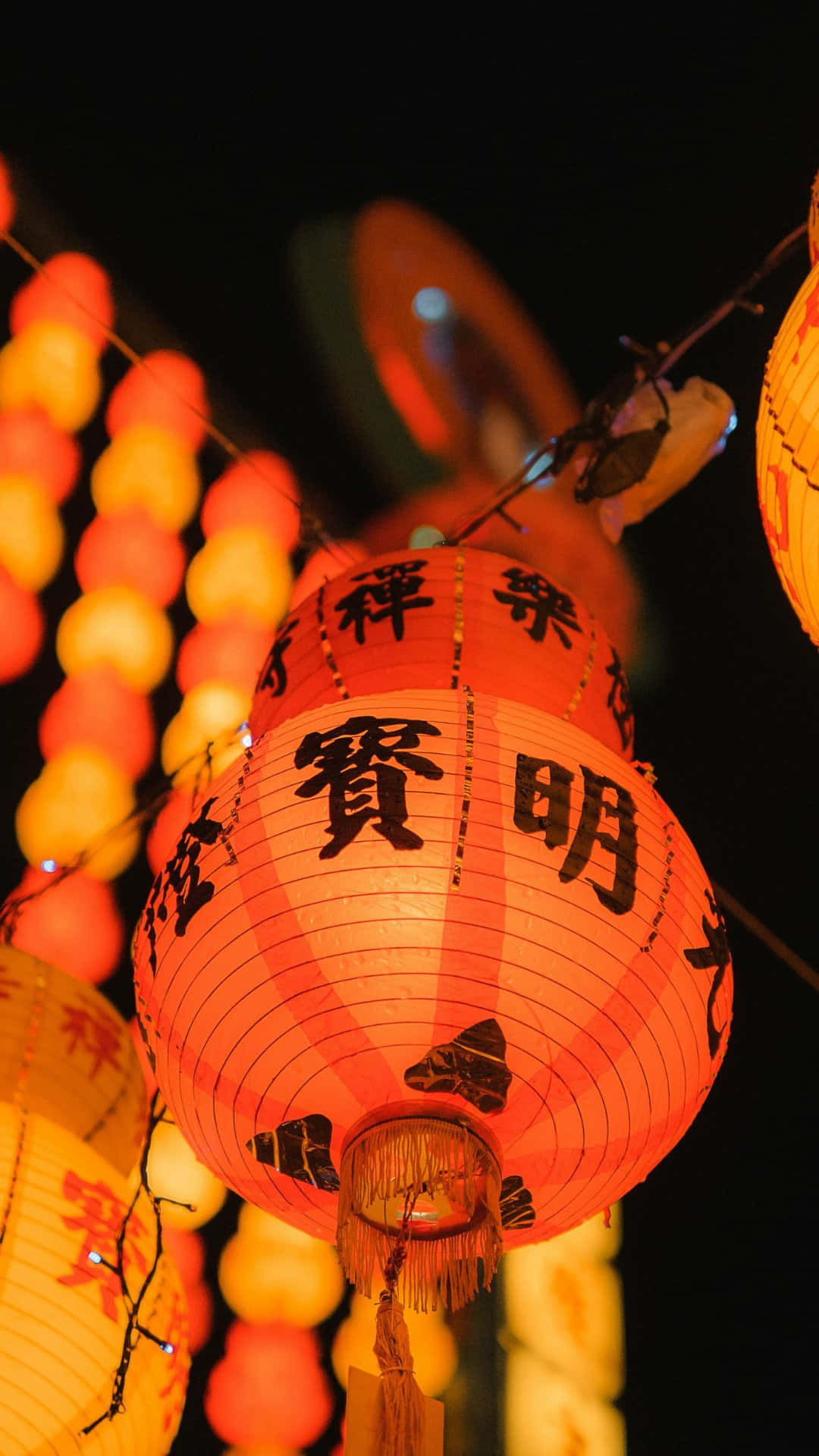  壁紙 — 鮮豔的橙色紙燈籠上帶有黑色中文字，在漆黑的夜空下溫暖地發光。