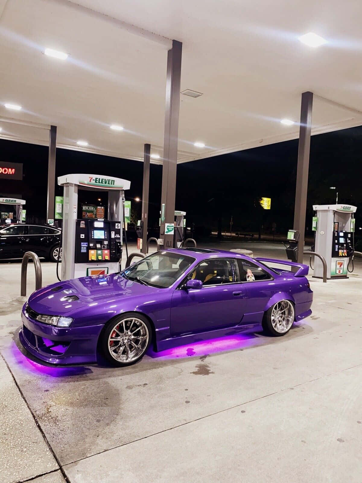  壁紙 — 一輛充滿活力的紫色改裝跑車，帶有發光底盤燈，夜晚停在7-Eleven附近的加油站。