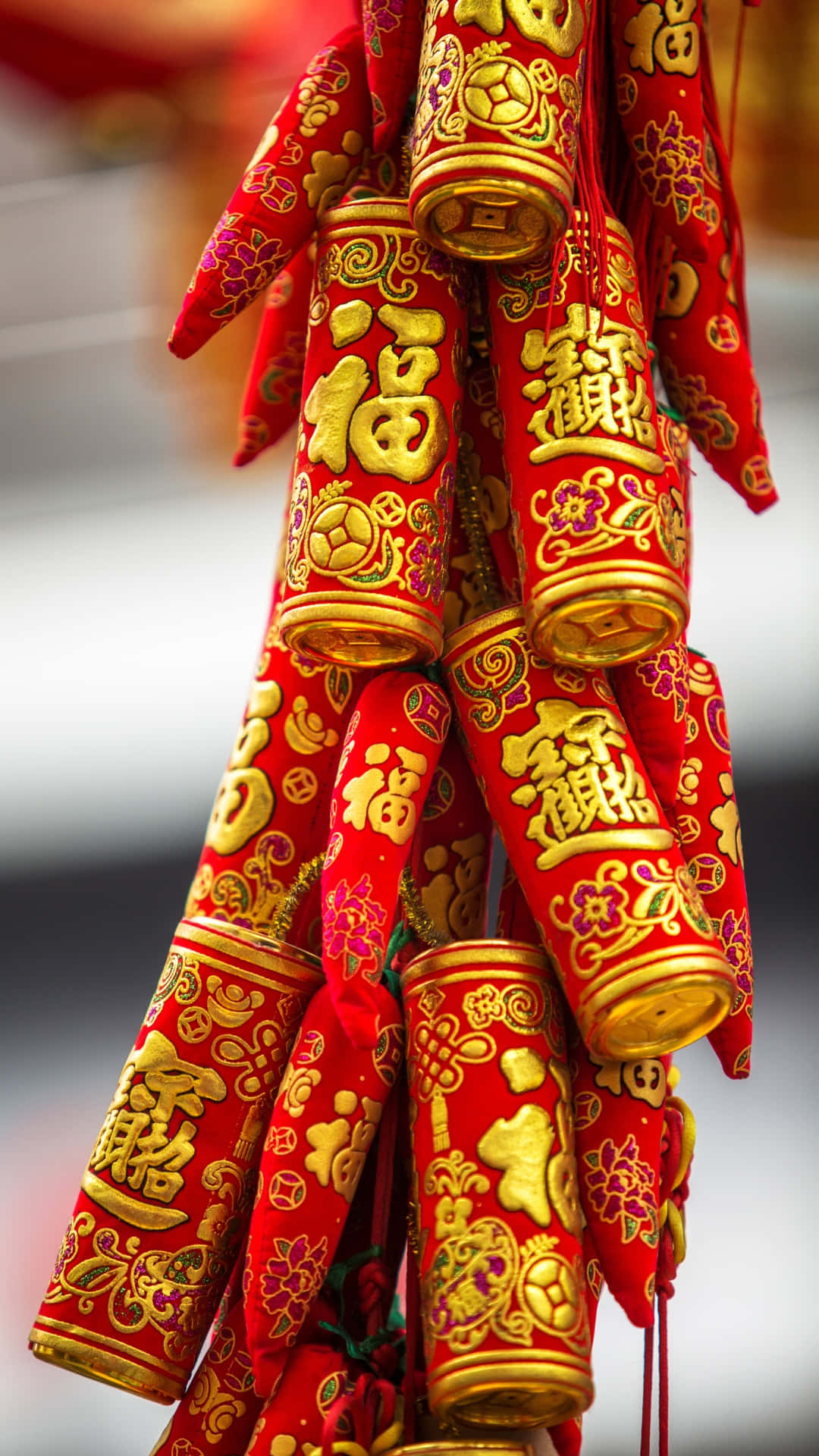  壁紙 — 鮮豔的紅色和金色中國鞭炮，飾有複雜的字符和花卉圖案，掛在節日的簇中。