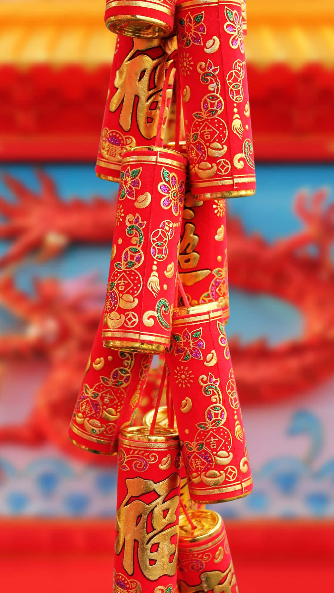  壁紙 — 鮮豔的紅色和金色中國鞭炮，飾有複雜的花卉圖案和幸運字符，在模糊的龍背景下喜慶地懸掛著。