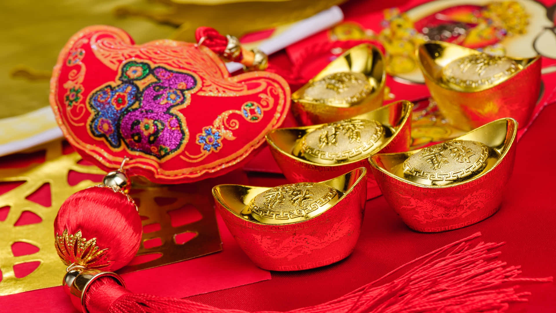  壁紙 — 鮮豔的紅色和金色中國新年裝飾，包括刺繡小袋和金錠，排列在節日布料上。