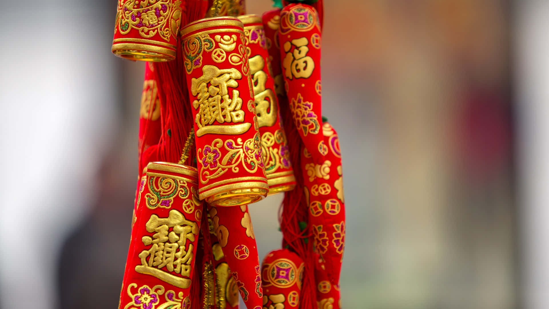  壁紙 — 鮮豔的紅色和金色中國新年裝飾流蘇，帶有複雜的書法，懸掛在柔和的模糊背景中。