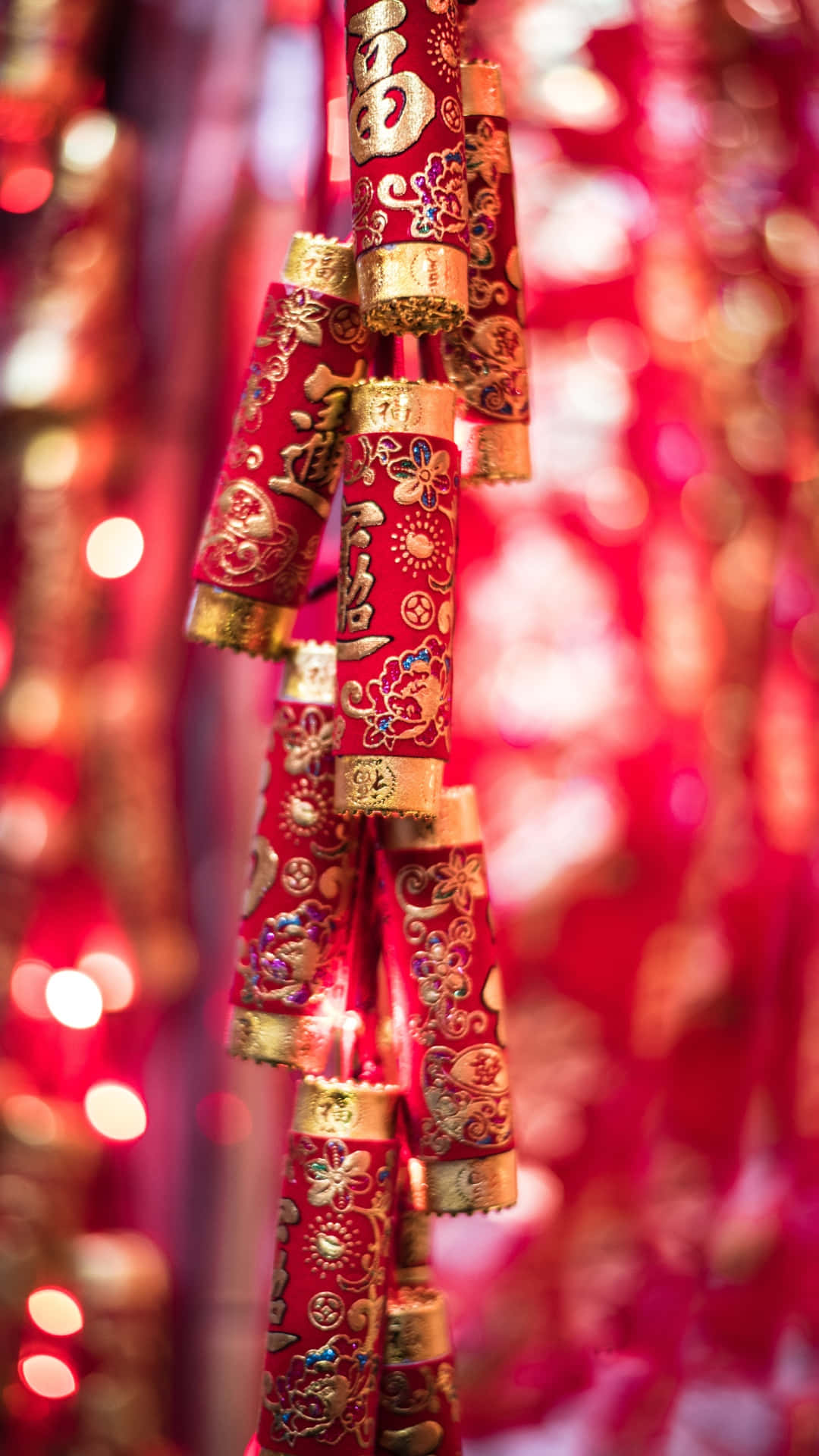  壁紙 — 鮮豔的紅色和金色中國新年鞭炮懸掛在節日般的發光燈光模糊中。