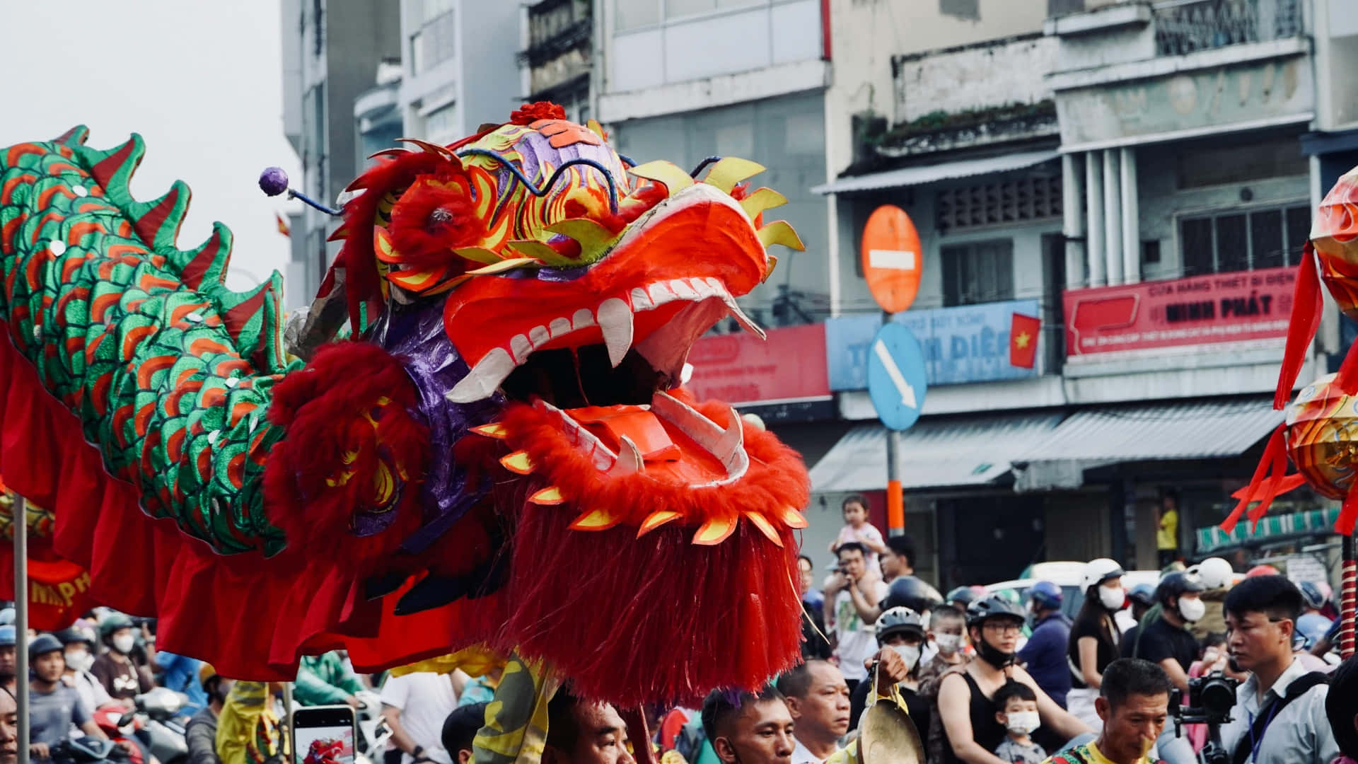  壁紙 — 鮮豔的紅綠舞龍服裝在白天節日期間於擁擠的城市街道上表演。