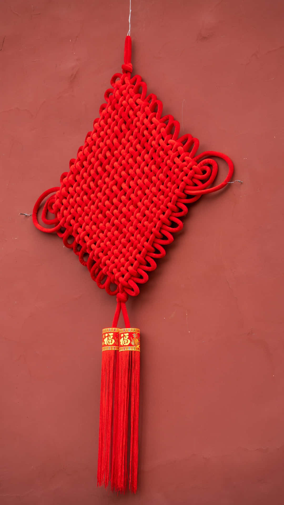  壁紙 — 一個鮮紅色的中國結飾品，帶有金色的「福」字流蘇，掛在質感豐富的赤陶牆上。