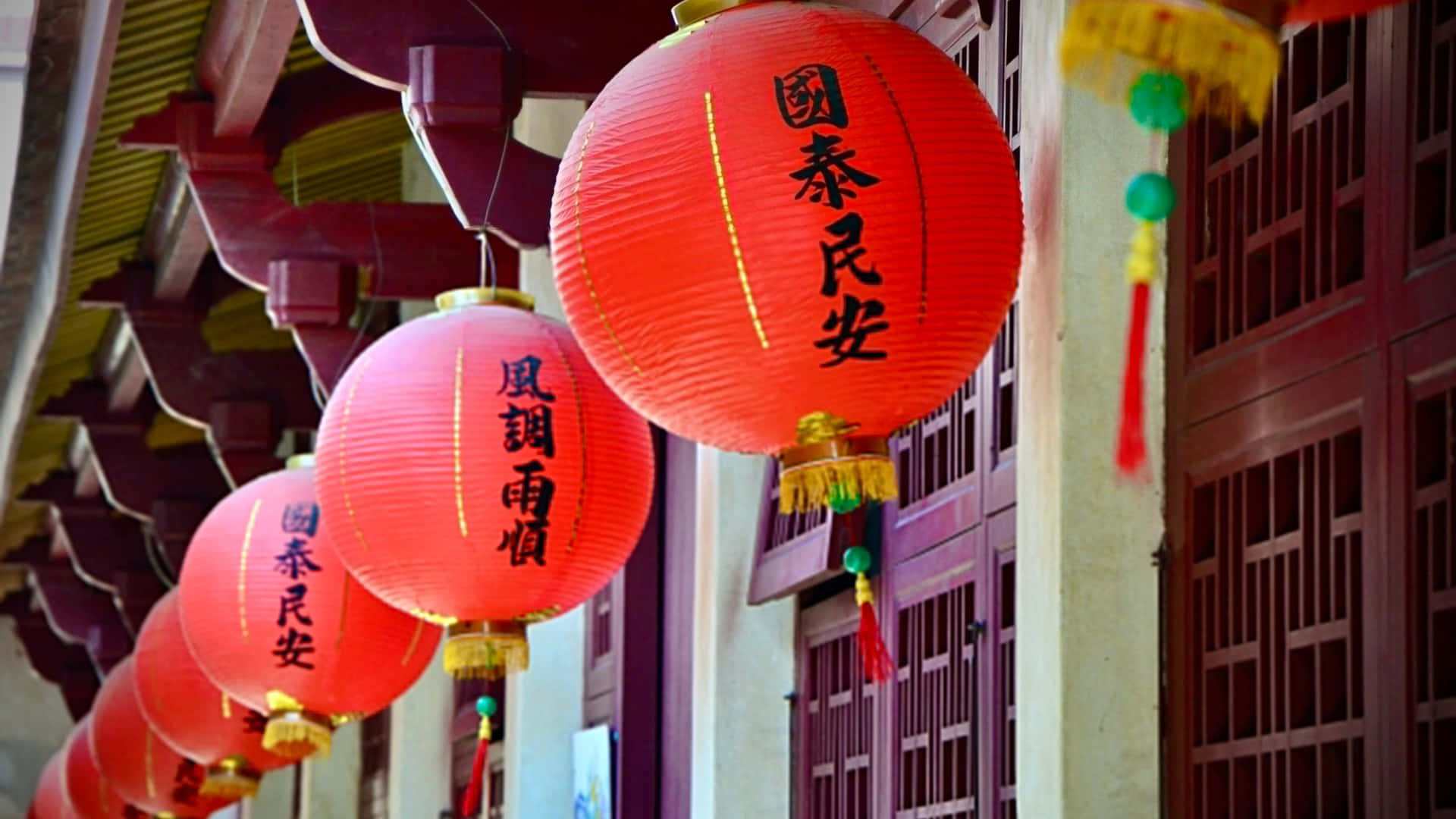  壁紙 — 鮮豔的紅色中國燈籠上帶有黑色書法，掛在一排傳統木建築前。