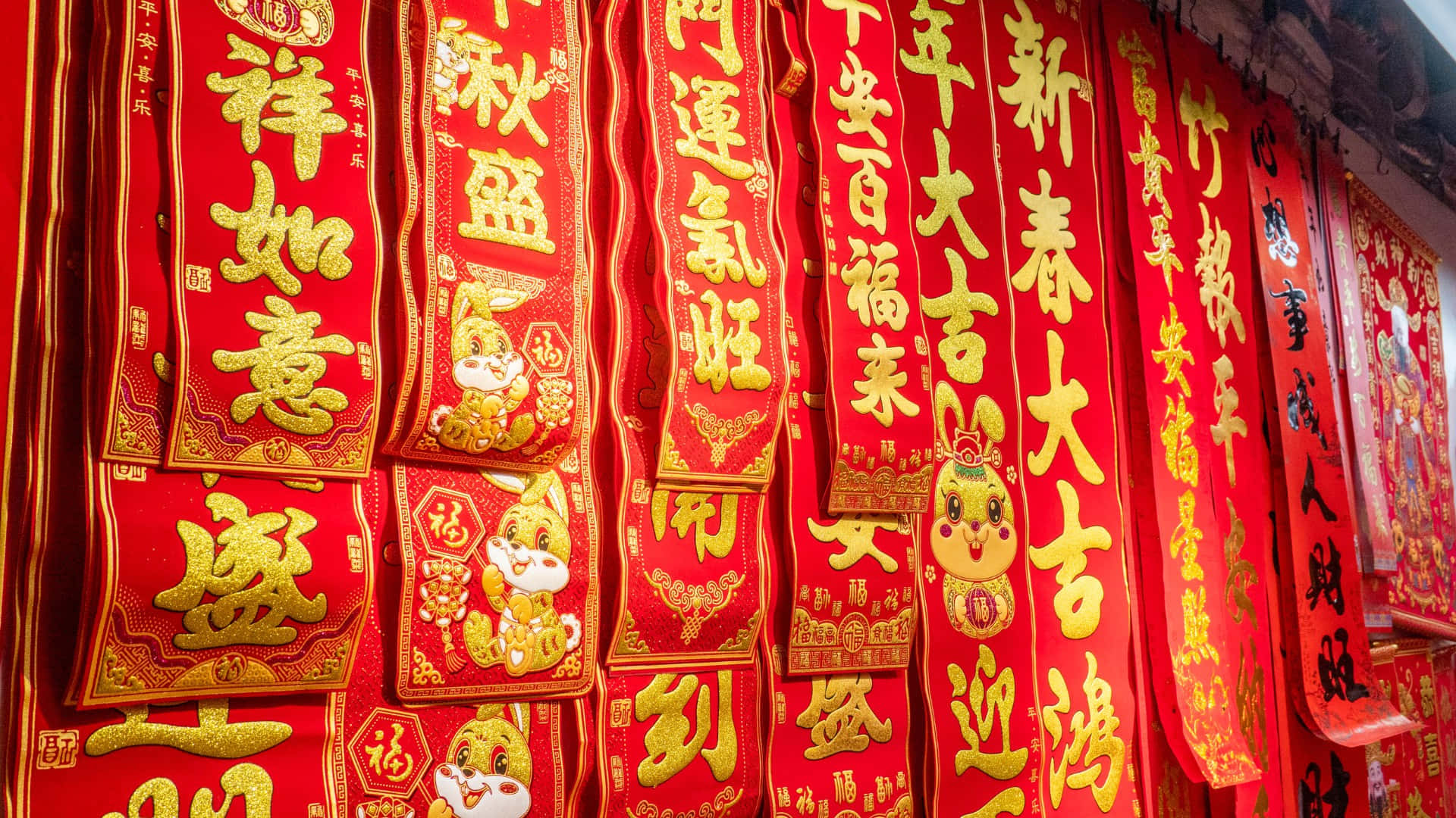  壁紙 — 鮮豔的紅色中國新年對聯，帶有金色書法和兔子圖案，密集地掛在節日展示中。