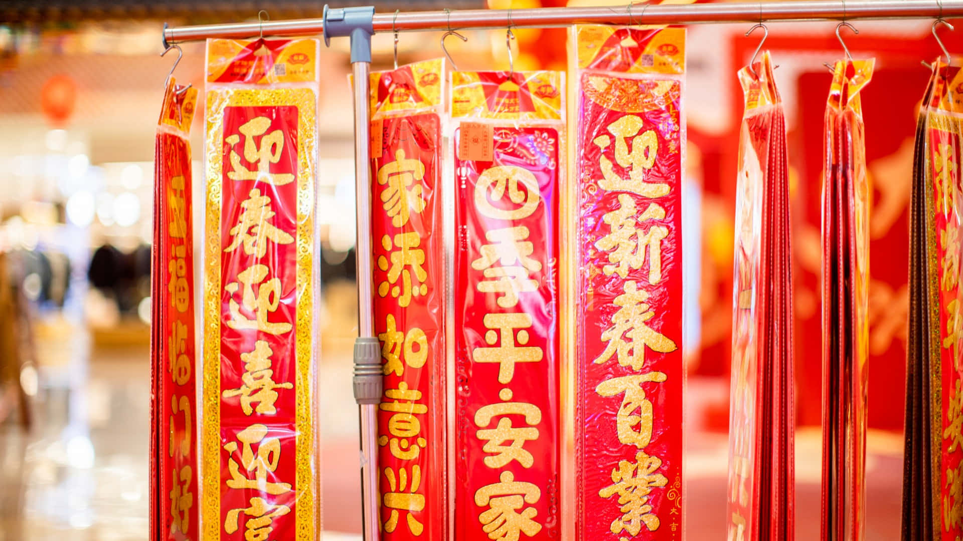  壁紙 — 鮮豔的紅色中國春聯配上金色書法，掛在節日市場攤位上。