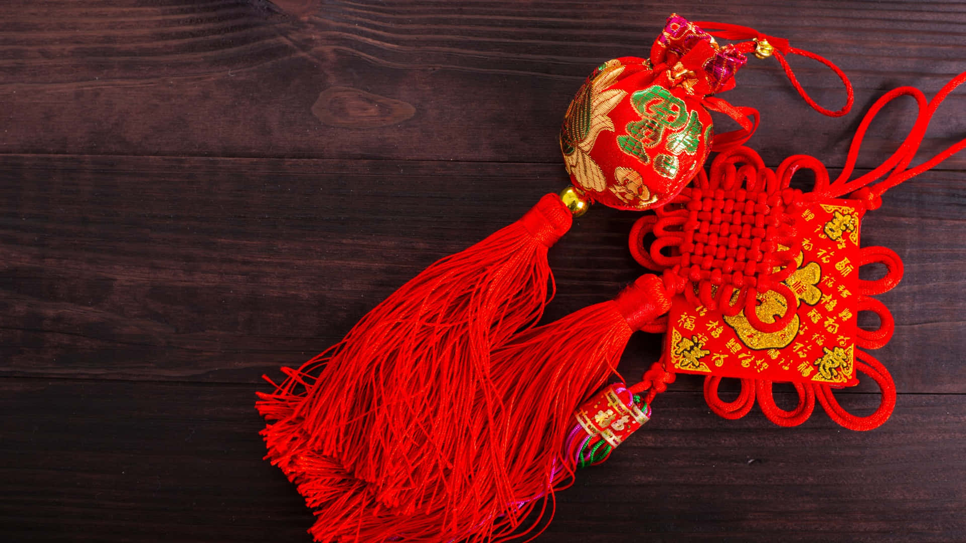  壁紙 — 鮮豔的紅色中國新年裝飾品，帶有金色刺繡和流蘇，放置在深色木質表面上。