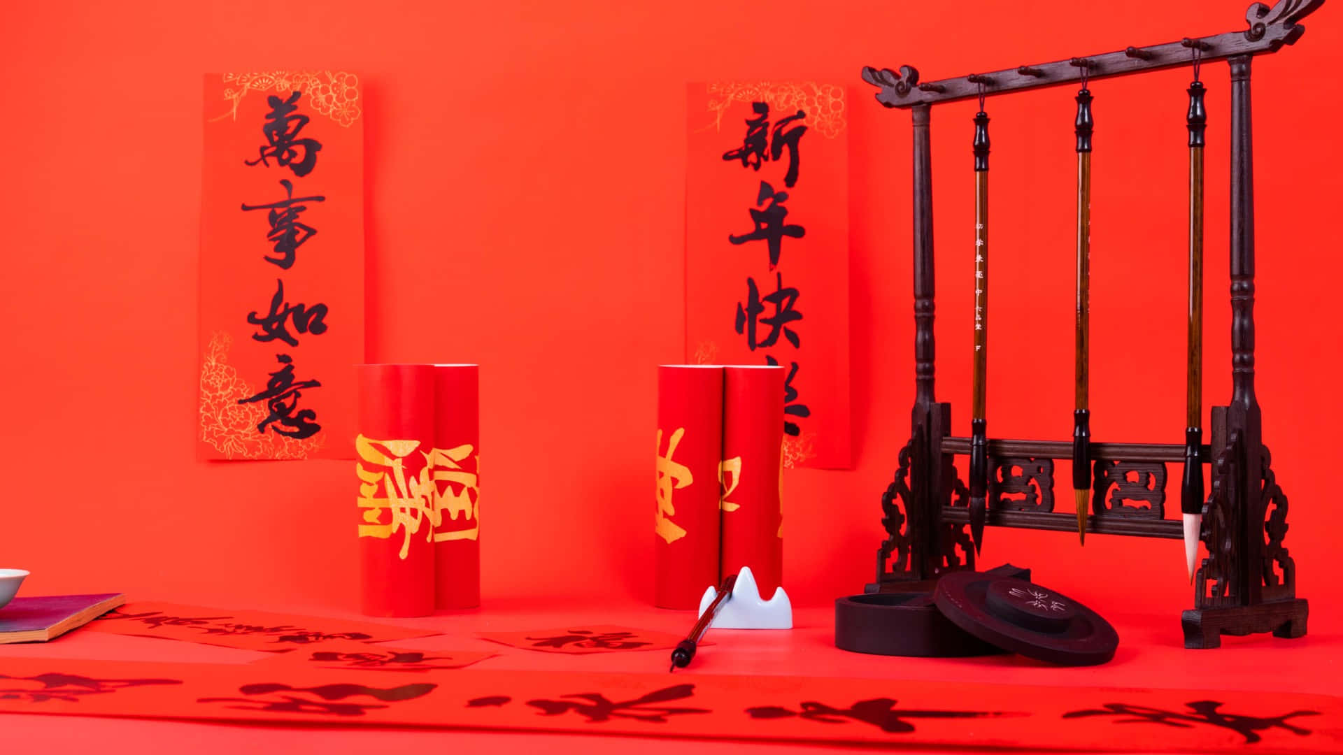  壁紙 — 充滿活力的紅色中國新年佈置，配有書法卷軸、筆架和硯台，背景為大膽的紅色。