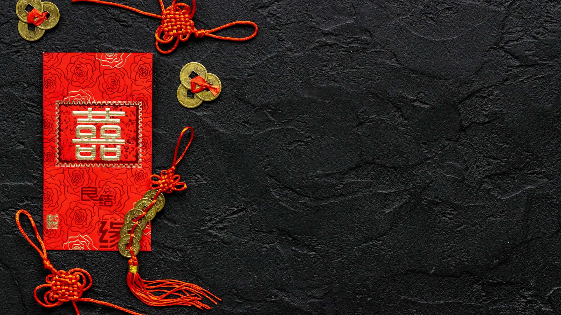  壁紙 — 一個鮮紅色的中式婚禮利是封，飾有金幣和精緻的繩結，放置在帶有紋理的黑色表面上。