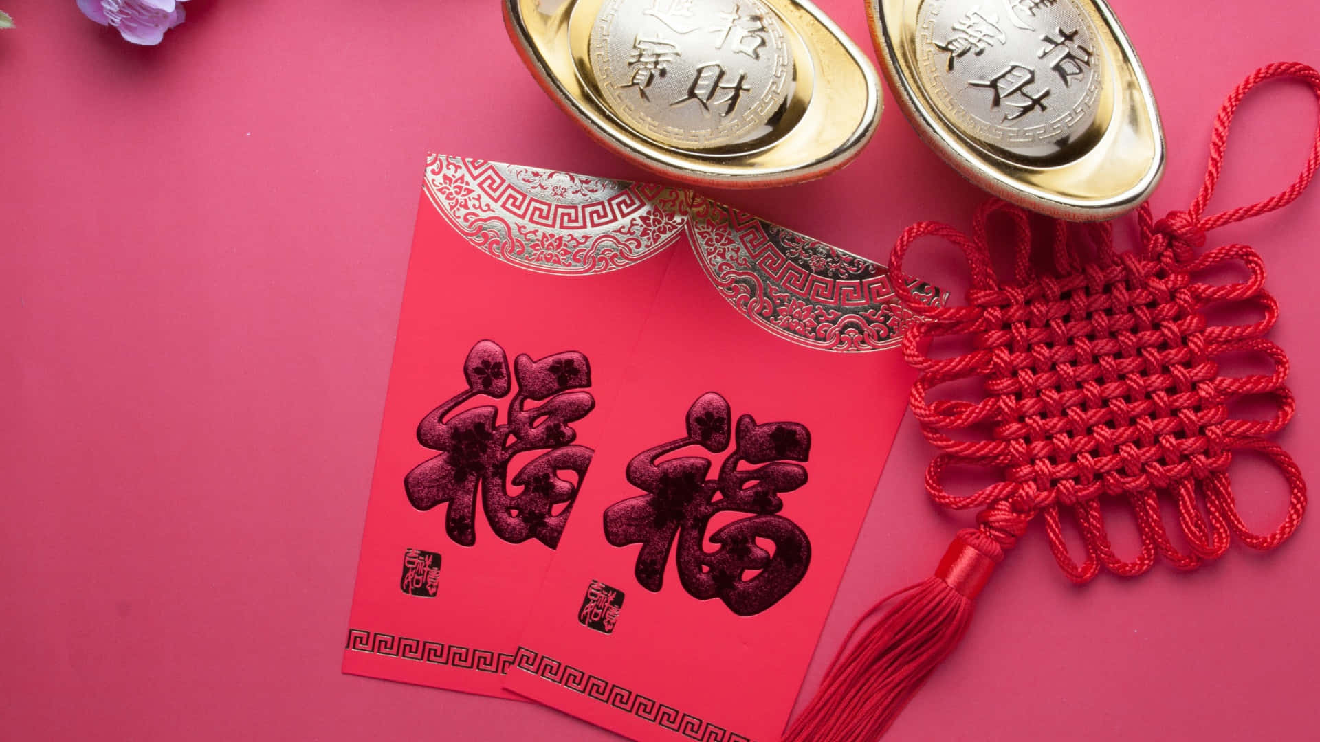  壁紙 — 鮮豔的紅色利是封上印有粗體黑色中文字，旁邊放著金元寶和紅色中國結，背景為相配的粉紅色。