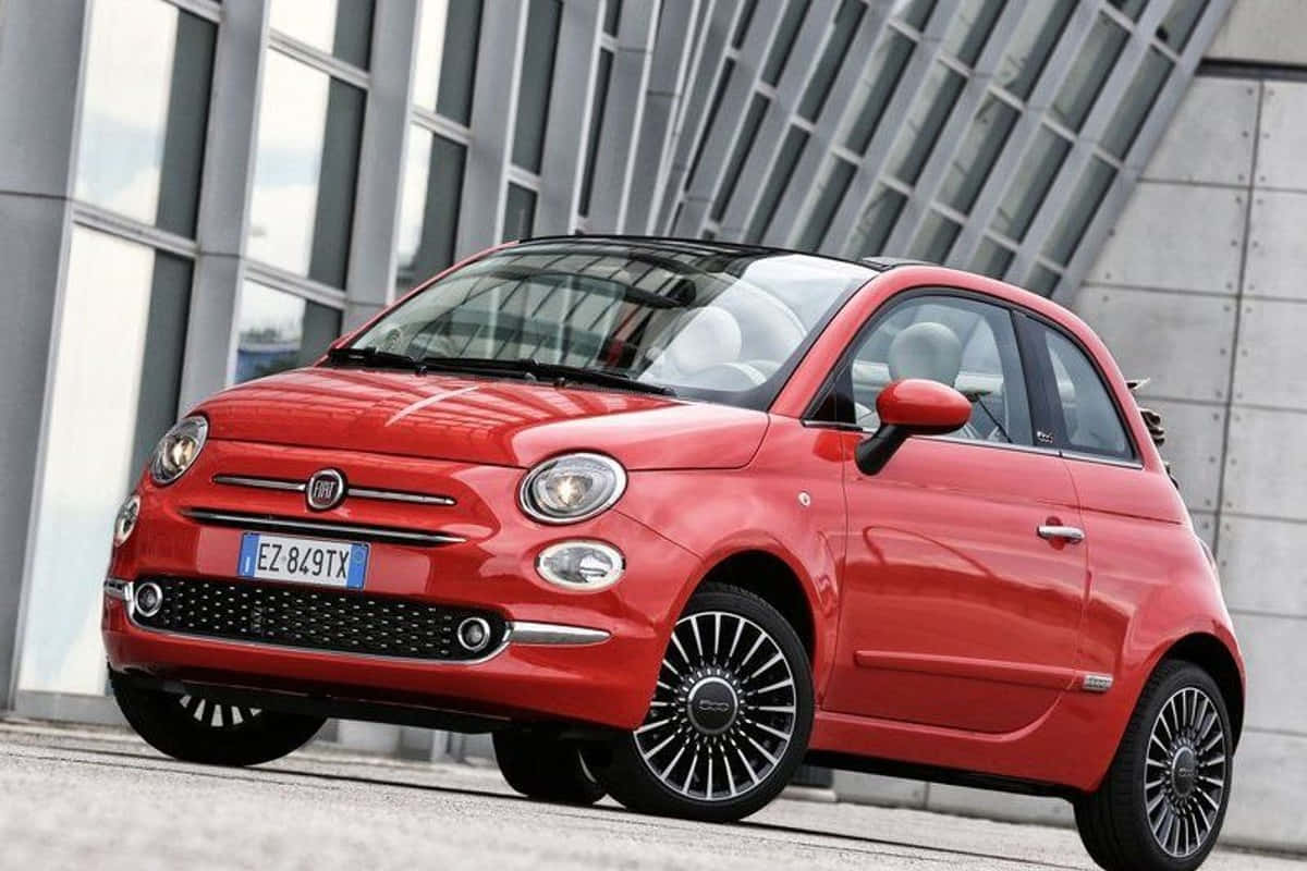 Fiat 500 桌布 壁紙 — 一輛鮮紅色的菲亞特500停在一棟幾何建築風格的現代玻璃和鋼結構建築前。