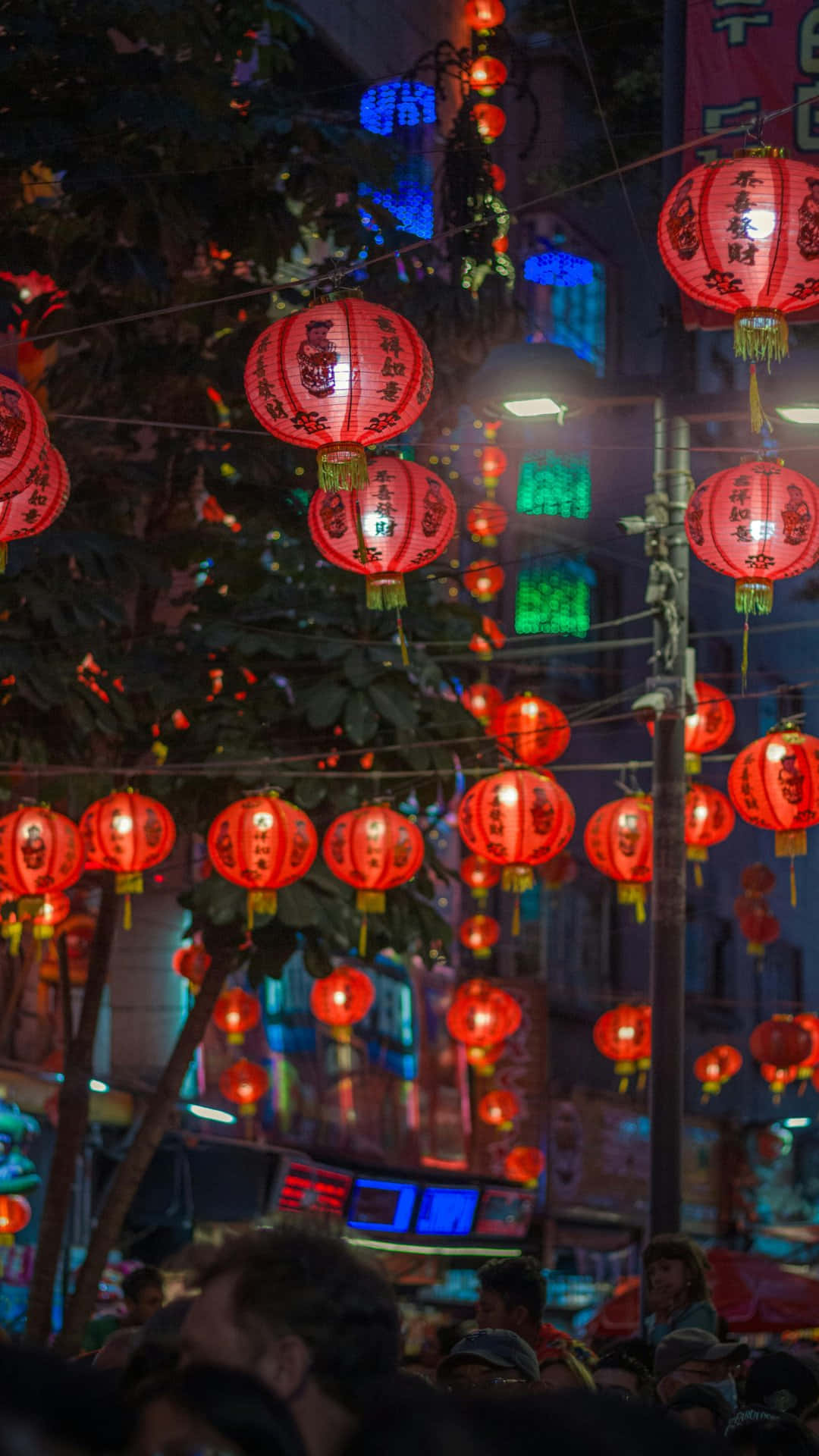  壁紙 — 鮮豔的紅色燈籠在熙熙攘攘的夜街上溫暖地發光，街上滿是人群和色彩繽紛的霓虹燈。