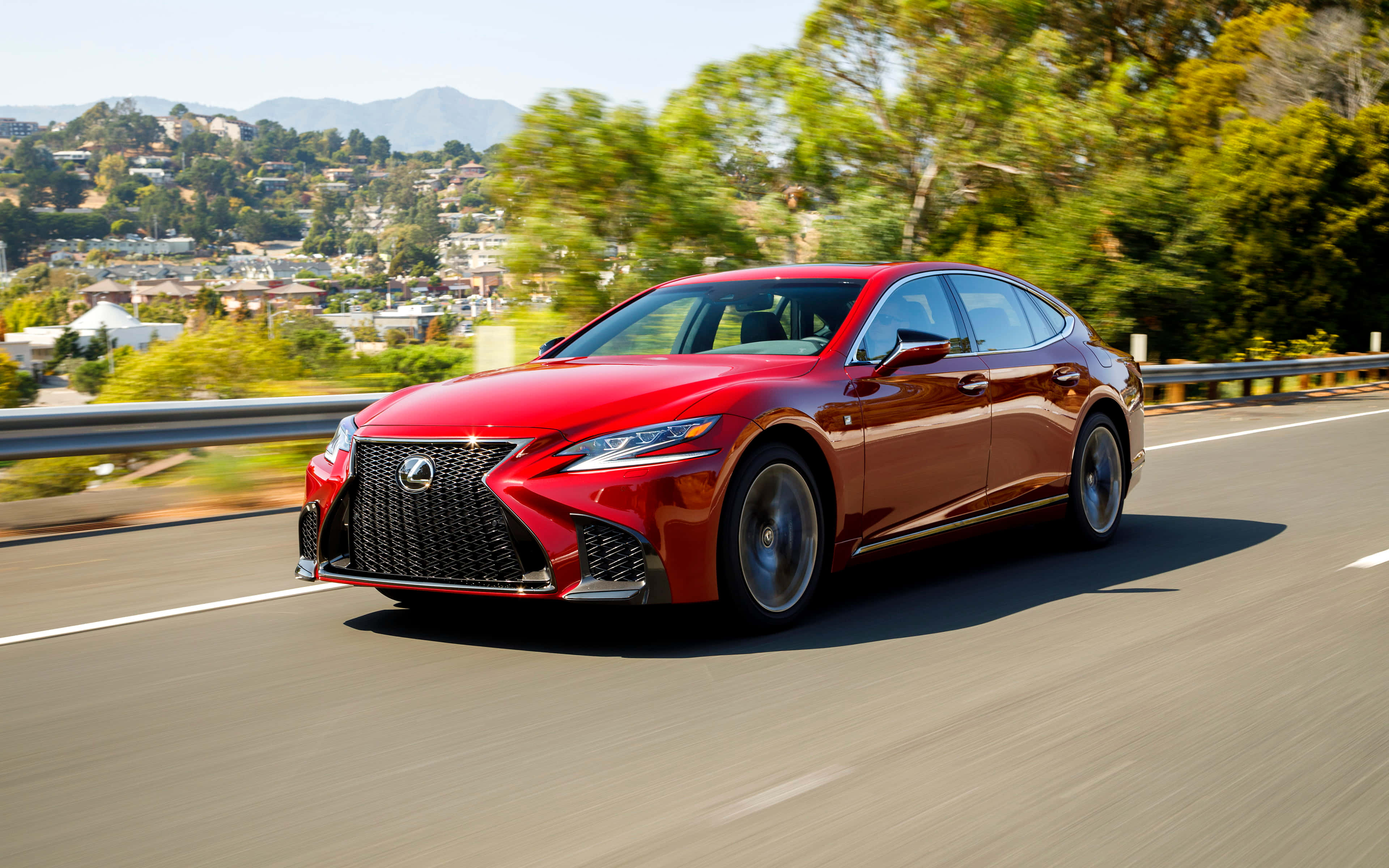 Lexus Ls 500 桌布 壁紙 — 一輛鮮紅色的凌志房車在陽光明媚的高速公路上疾馳，背景是模糊的綠樹和遠山。