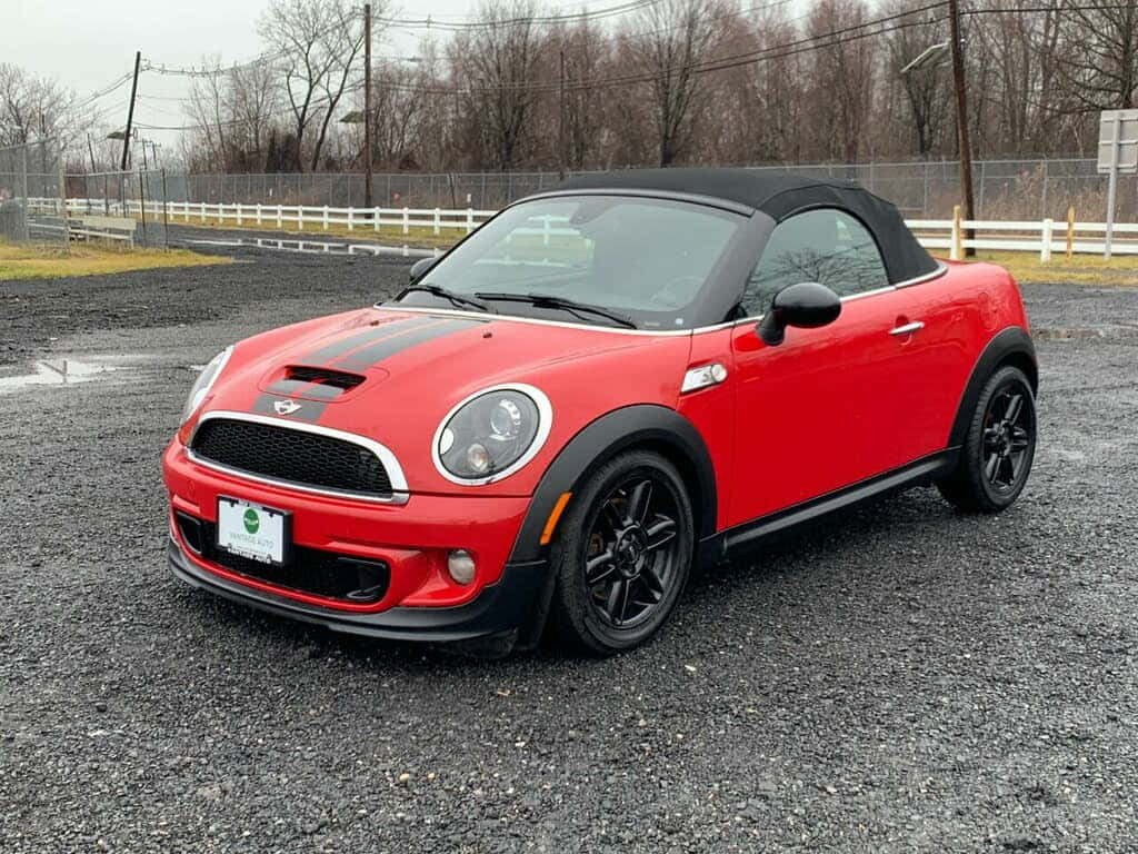  壁紙 — 一輛鮮紅色MINI Cooper開篷車，帶有黑色飾邊，停泊在碎石地上，天空多雲。