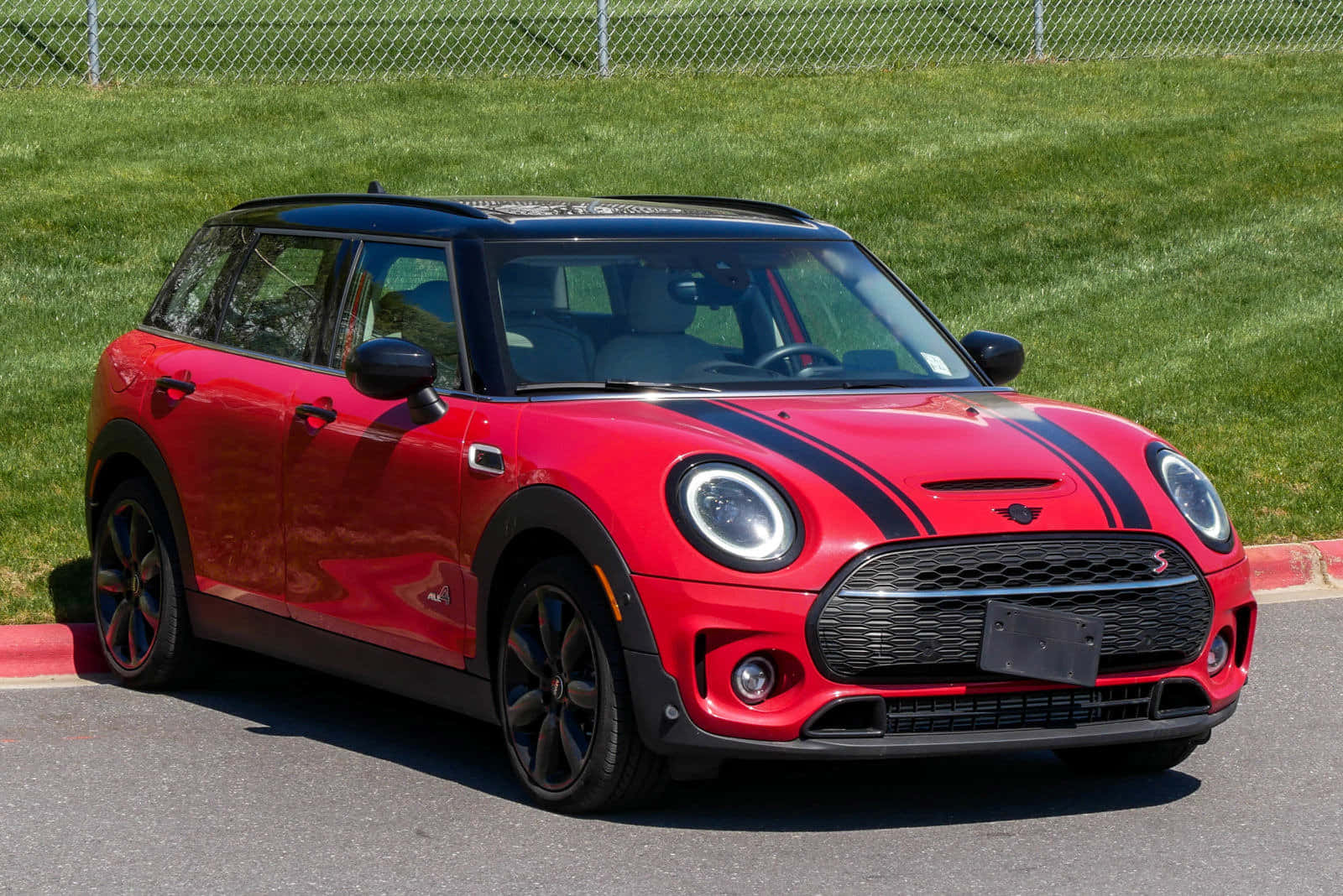 Mini Cooper S Clubman All4 桌布 壁紙 — 一輛鮮紅色的MINI Cooper S帶有黑色賽車條紋，停在陽光下草地斜坡旁的瀝青路上。