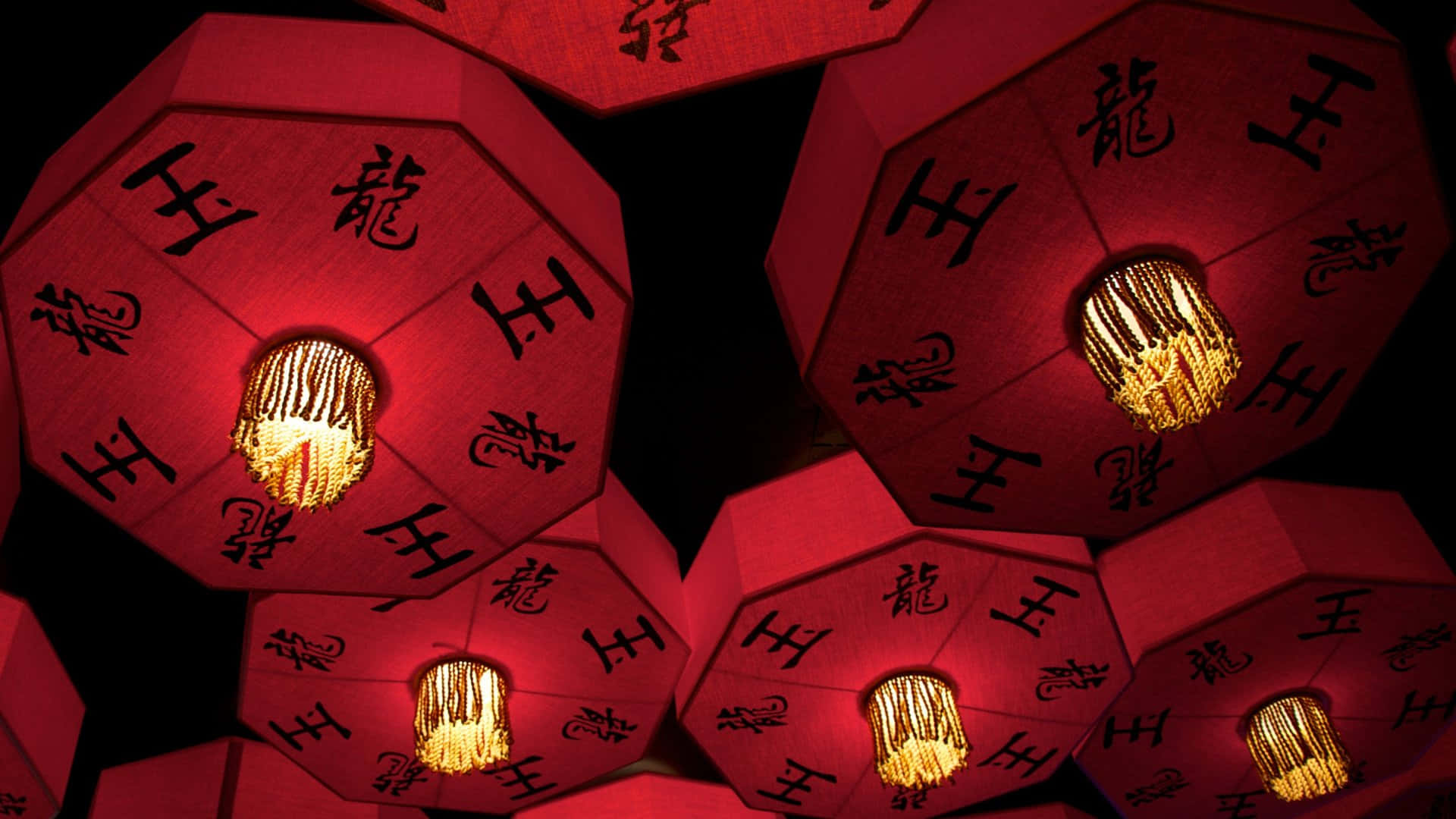  壁紙 — 鮮豔的紅色八角燈籠，帶有發光的金色流蘇和黑色中文字，在黑暗背景下閃耀。