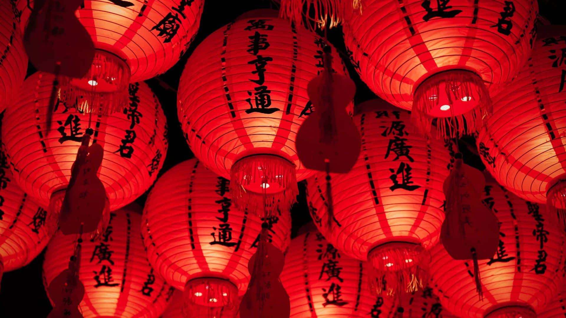  壁紙 — 鮮豔的紅色紙燈籠在黑暗的夜空中溫暖地發光，裝飾著優雅的黑色中國書法。