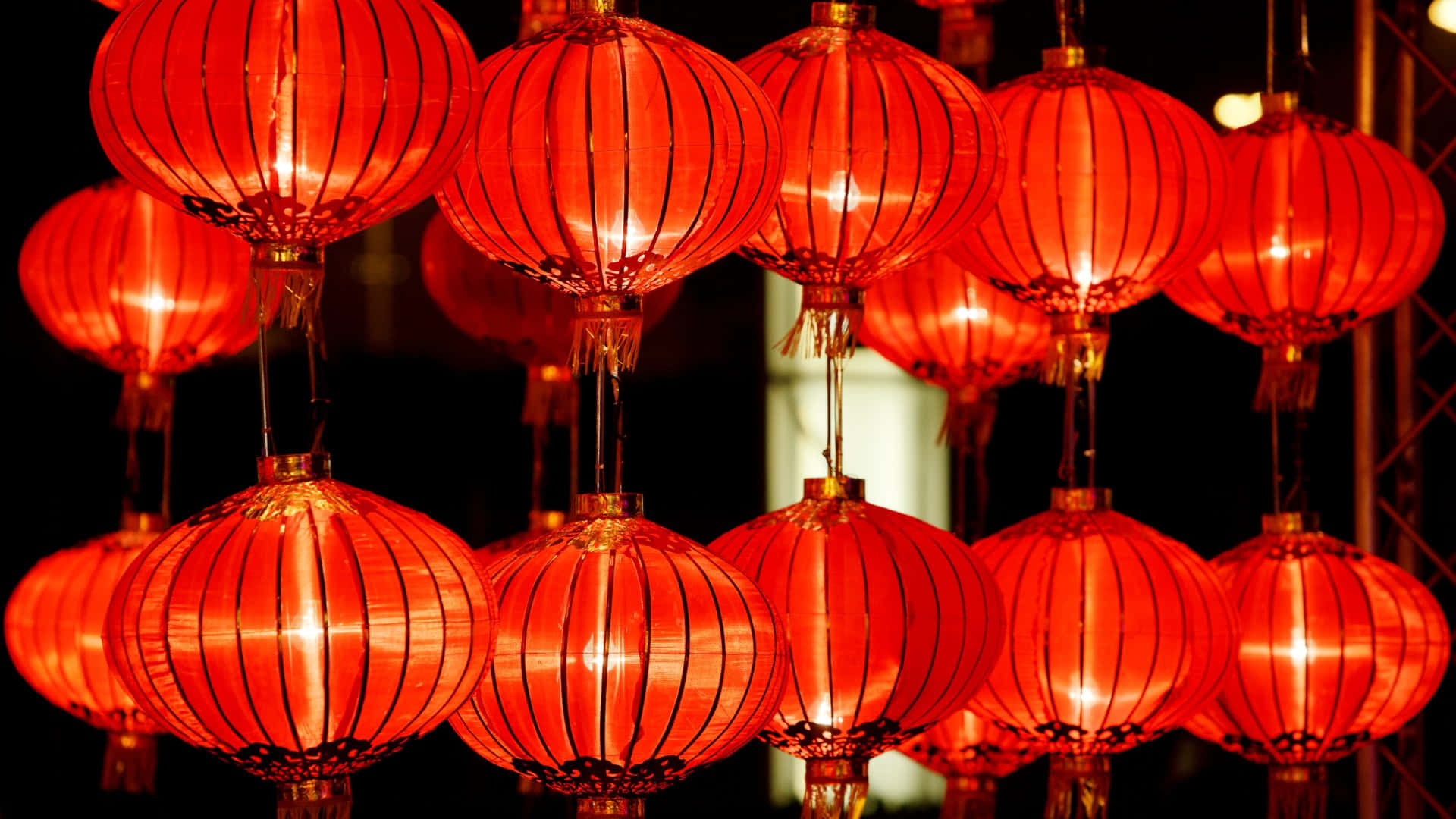  壁紙 — 鮮豔的紅色紙燈籠在漆黑的夜空中溫暖地發光，投射出柔和的光線，營造出節日氣氛。