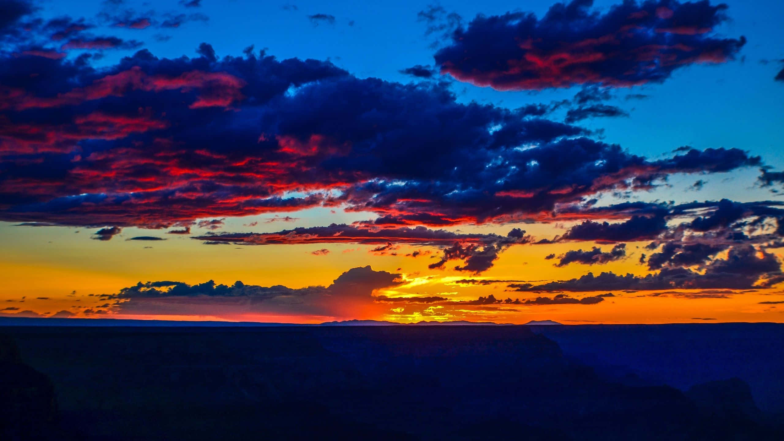 Colorful Sunset 桌布 壁紙 — 充滿活力的日落將雲彩染成火紅和橙色，映照在暮色中深藍色的峽谷之上。
