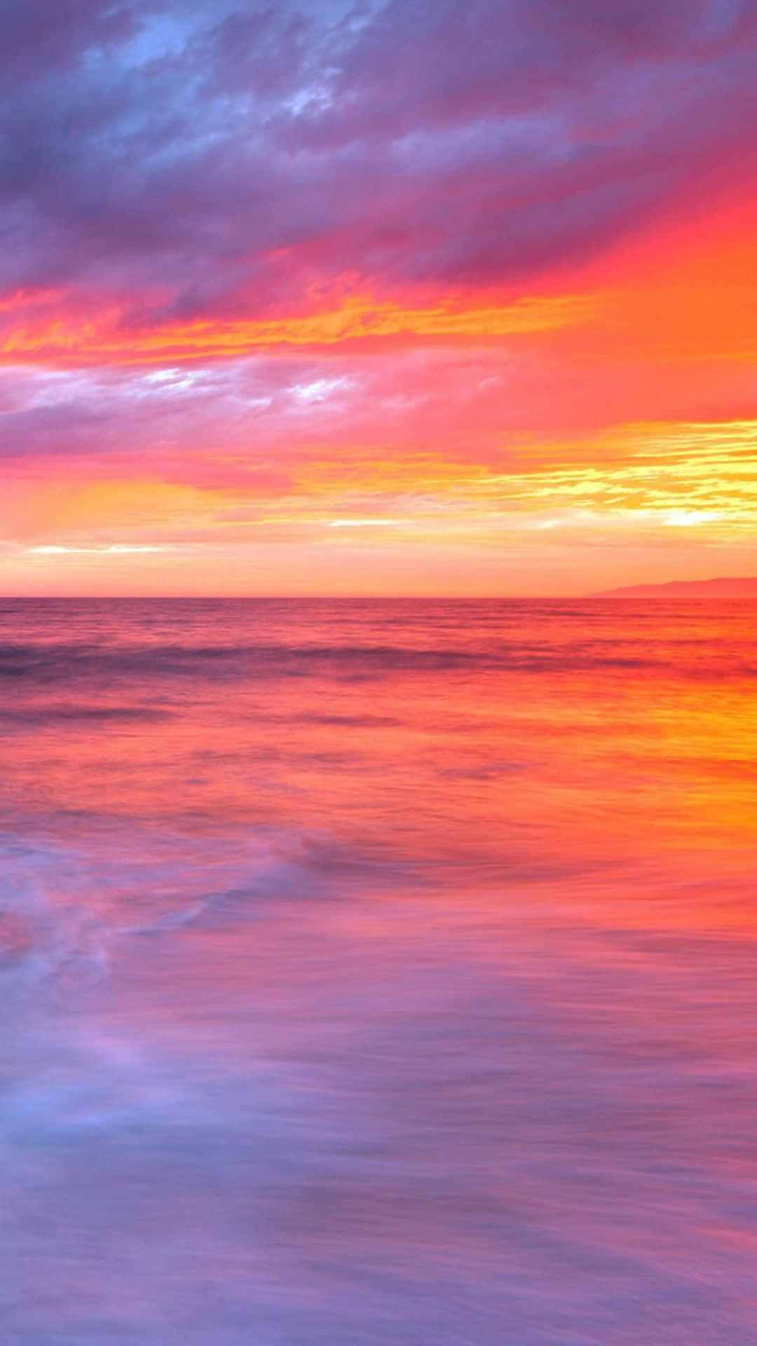 Colorful Sunset 桌布 壁紙 — 充滿活力的日落將海洋染成火熱的橙色和紫色色調，海浪輕輕地湧向海岸。