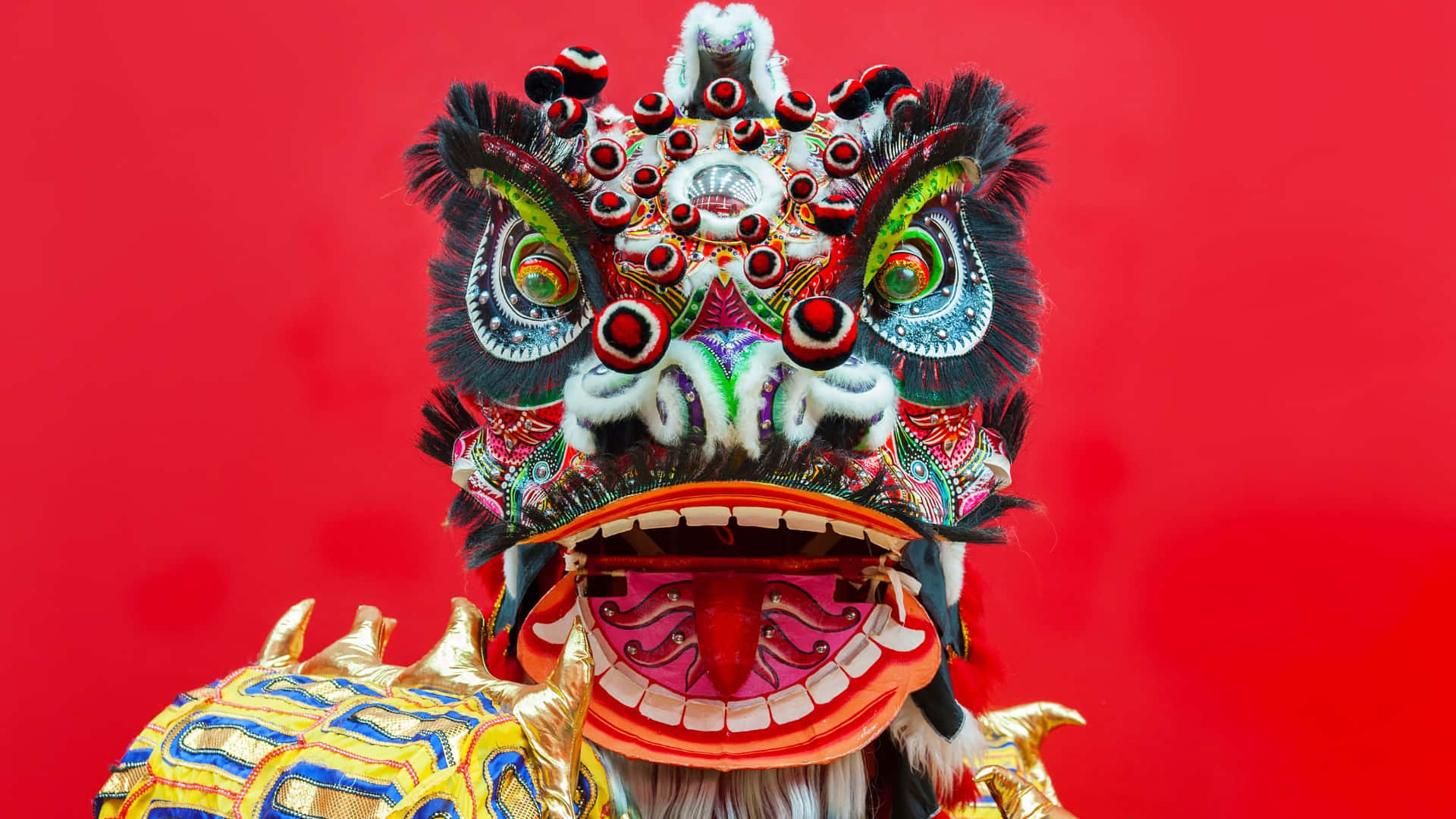  壁紙 — 色彩鮮豔的傳統中國舞獅面具，帶有精緻圖案和鮮明色彩，襯托在生動的紅色背景上。
