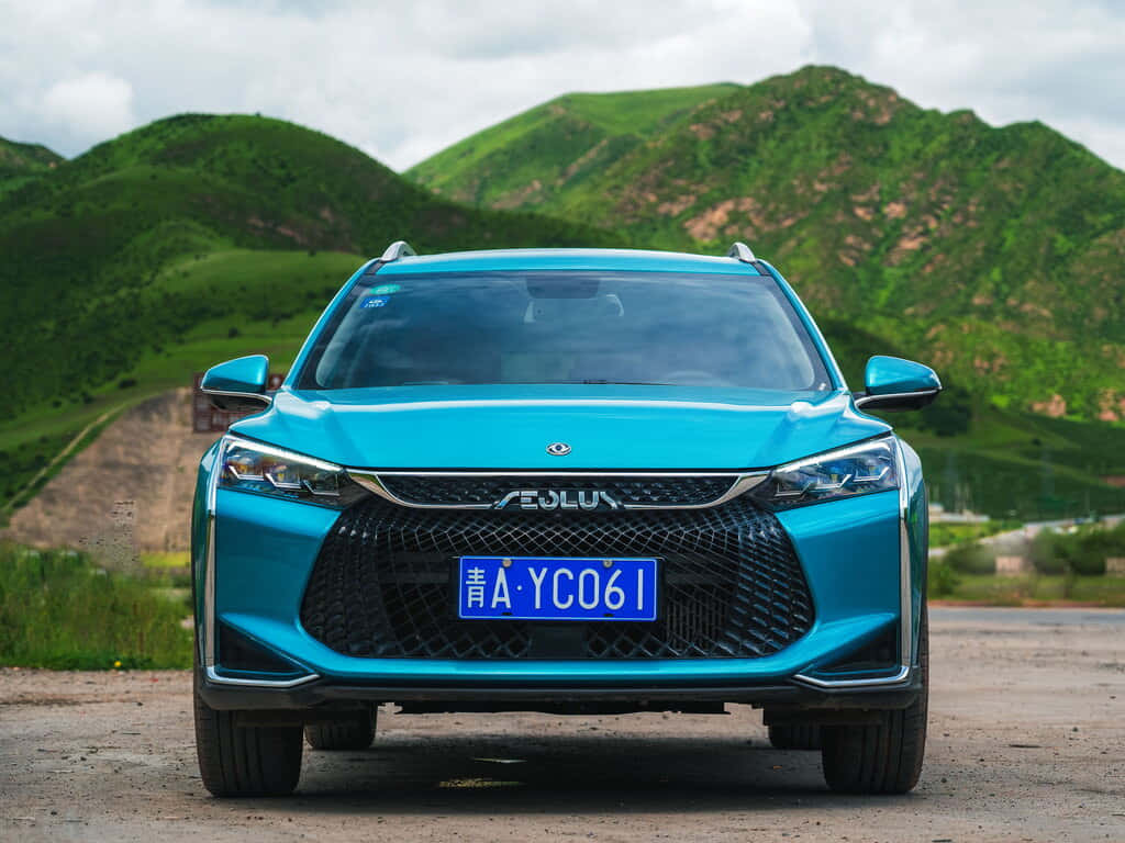  壁紙 — 一輛充滿活力的藍綠色SUV在泥路上向前行駛，背景是茂密的綠色山丘和陰天。
