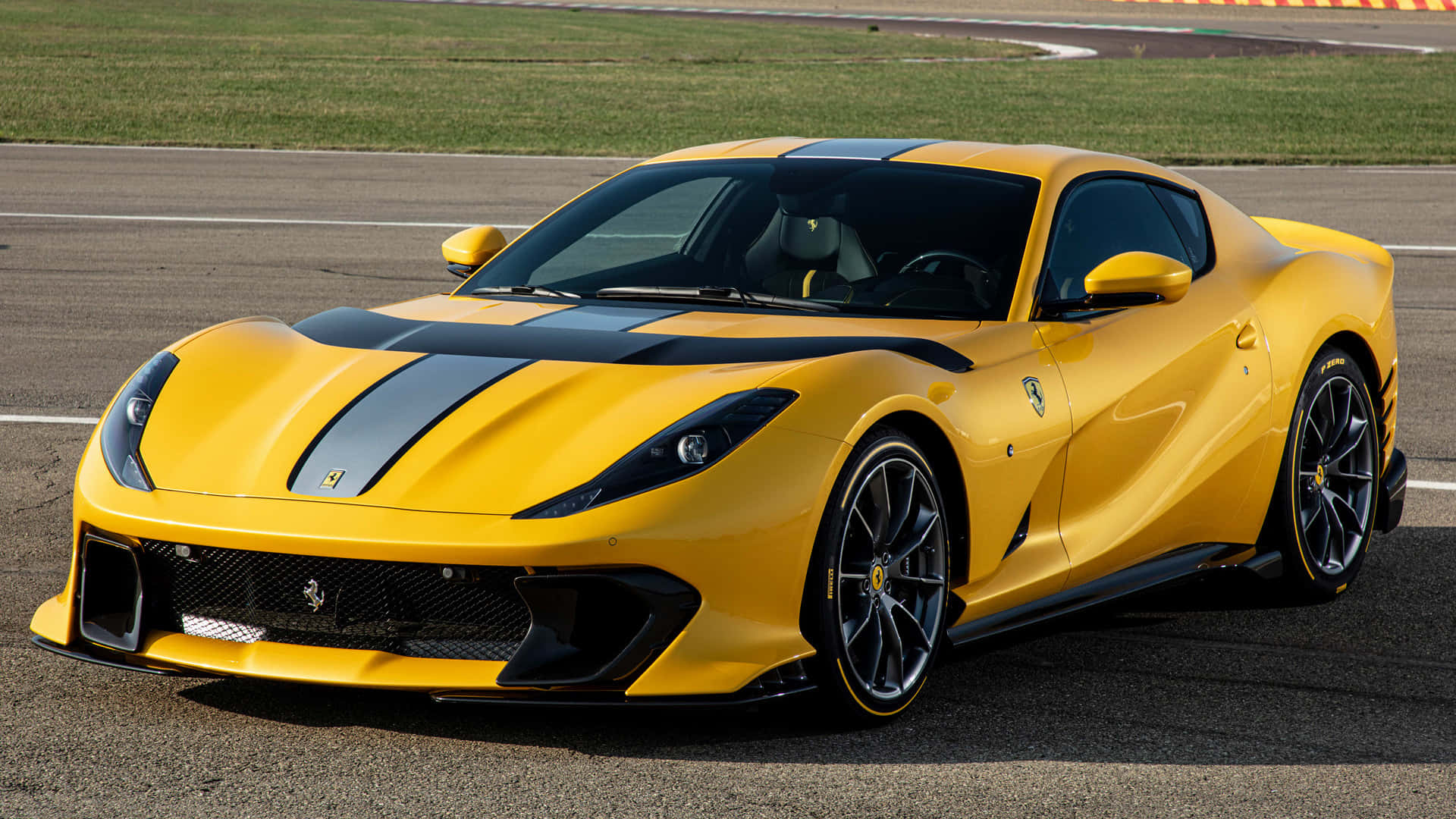 Ferrari 812 Superfast 桌布 壁紙 — 一輛充滿活力的黃色法拉利跑車，帶有黑色賽車條紋，在明亮的日光下停放在賽道上。