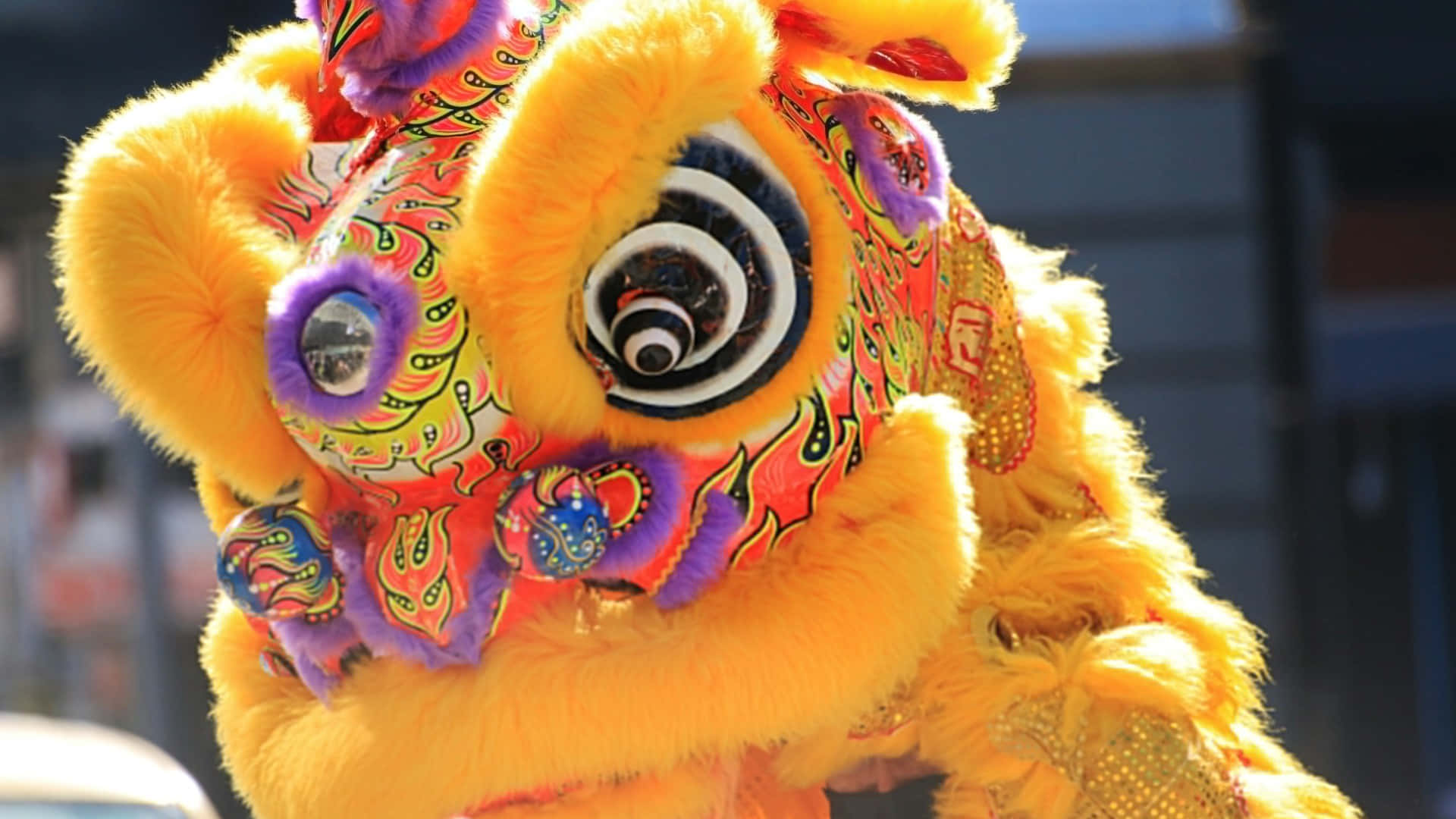  壁紙 — 鮮黃色舞獅服飾，帶有旋轉的紅色、紫色和金色圖案，在明亮的日光下閃耀。