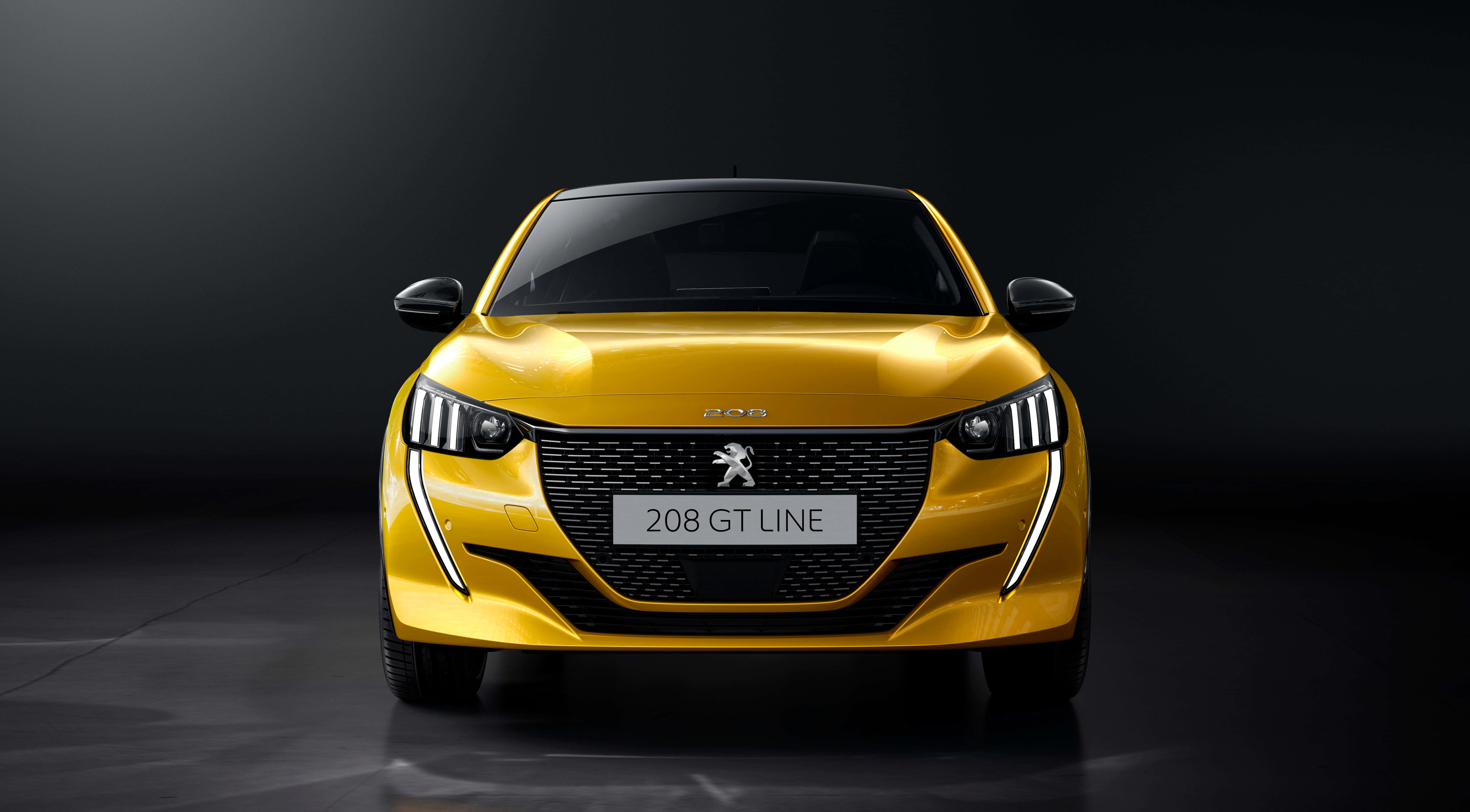 Peugeot 208 桌布 壁紙 — 一輛充滿活力的黃色Peugeot 208 GT Line在黑暗的攝影棚中正面朝前，戲劇性的燈光凸顯其時尚現代設計。