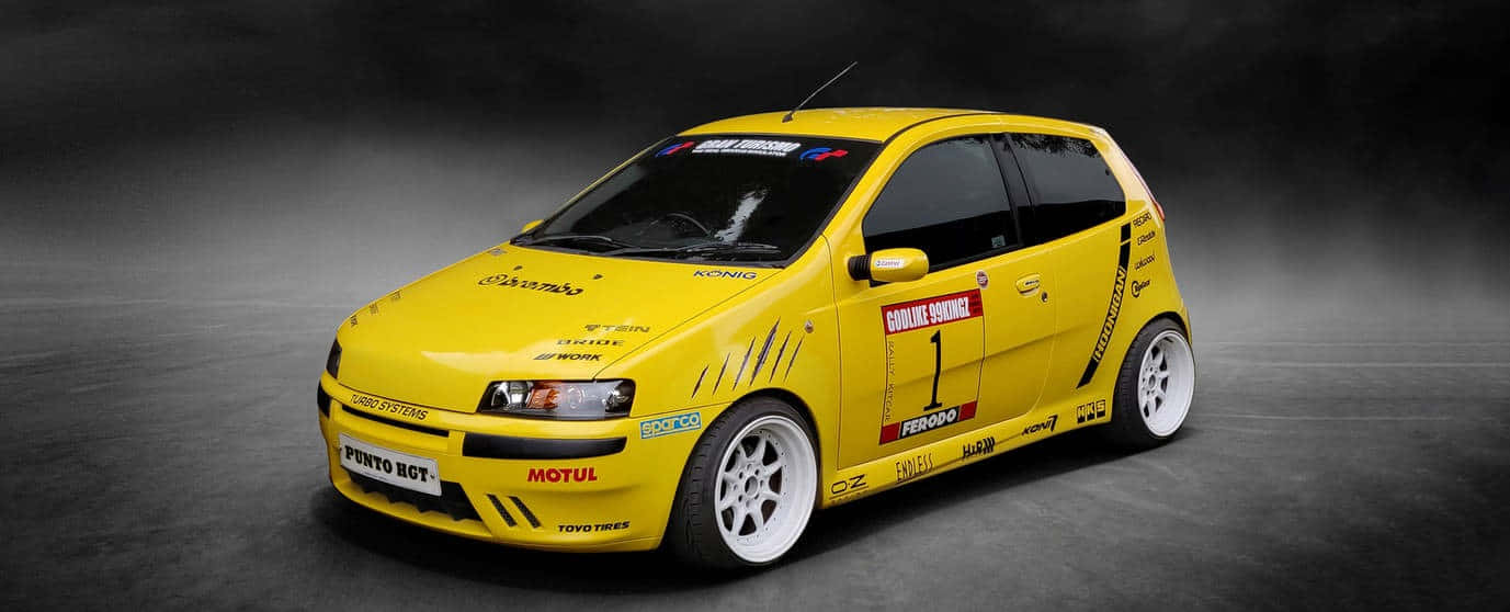 Fiat Punto 桌布 壁紙 — 一輛充滿活力的黃色拉力賽車，帶有賽車貼紙和白色輪圈，矗立在深色工作室地板上。
