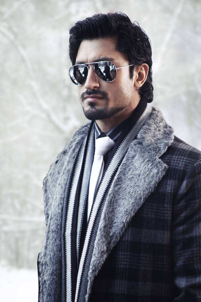 Vidyut Jamwal 穿冬季外套 壁紙 — 一位時尚男士穿著毛領格紋外套和飛行員太陽眼鏡，自信地站在雪景背景前。