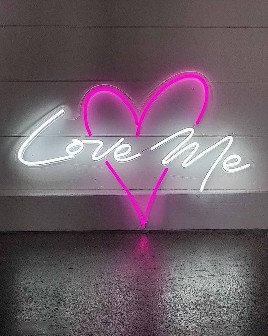粉紅色心形和白色「Love Me」霓虹燈牌在木牆上發光，地板有倒影。