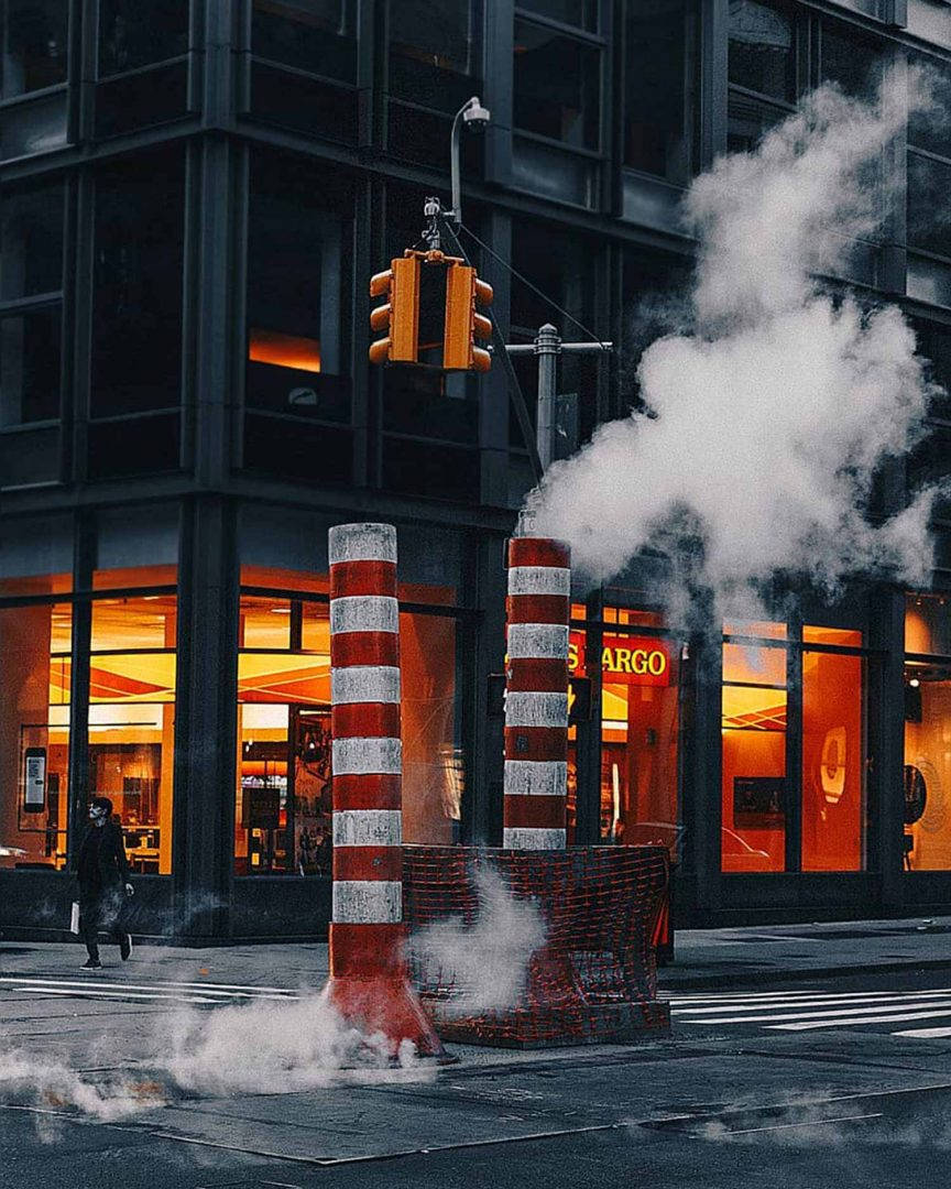 夜間城市中，發光商店櫥窗附近的建築屏障冒出蒸氣。