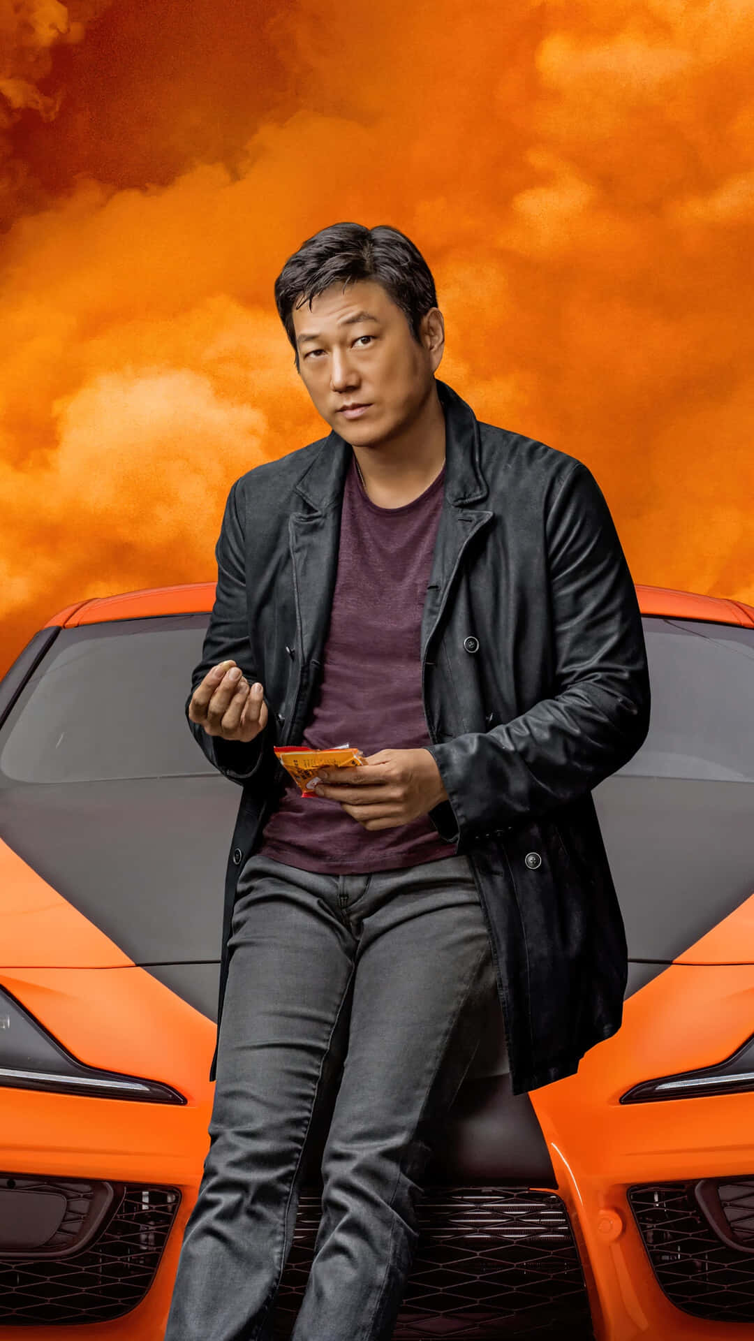 穿黑色外套的男子坐在橙色跑車引擎蓋上，橙色天空